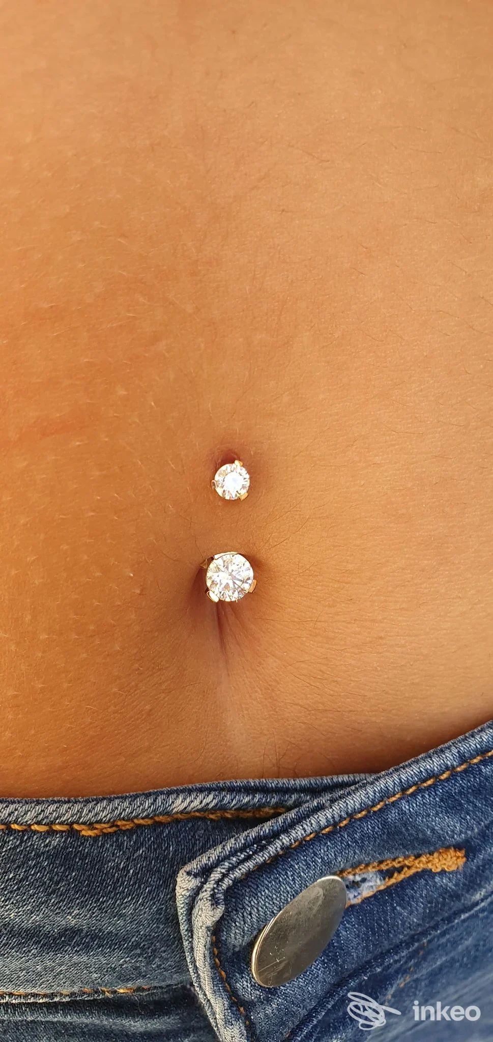 Piercing all'ombelico con due gioielli brillanti, foto di Body Factory a Trieste, dettaglio dell'addome e dei jeans.