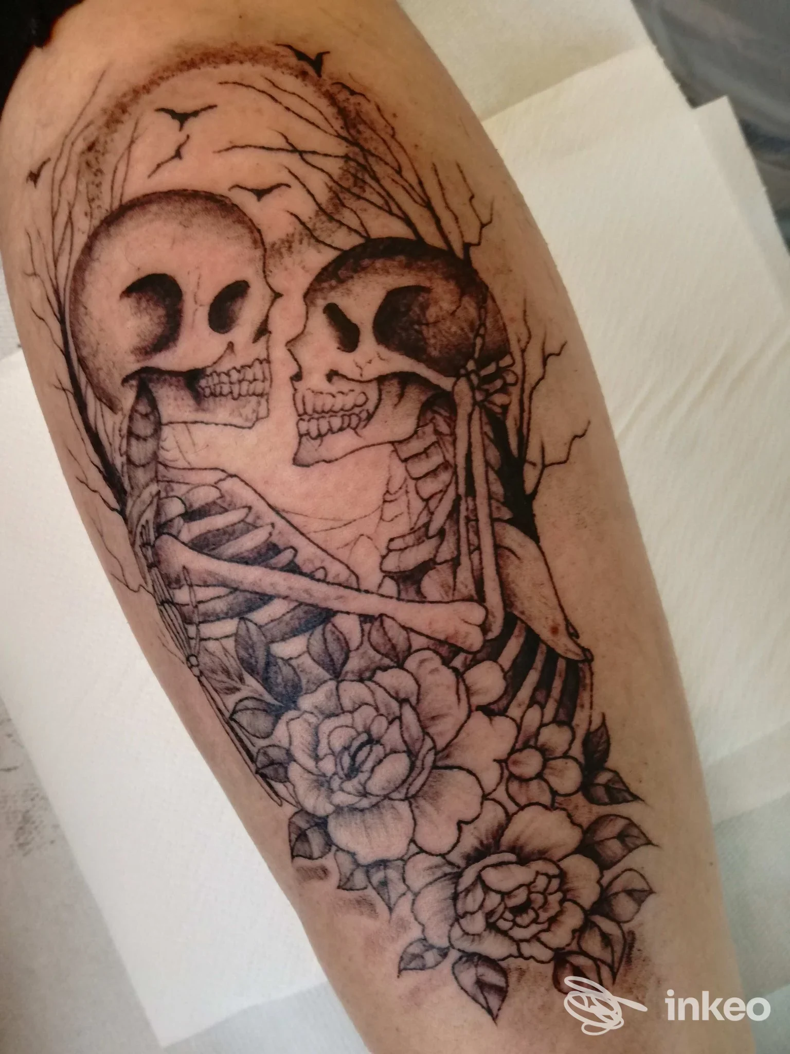 Tatuaggio su avambraccio con due scheletri abbracciati e rose in bianco e nero. Sunflower Tattoo, Basiliano.