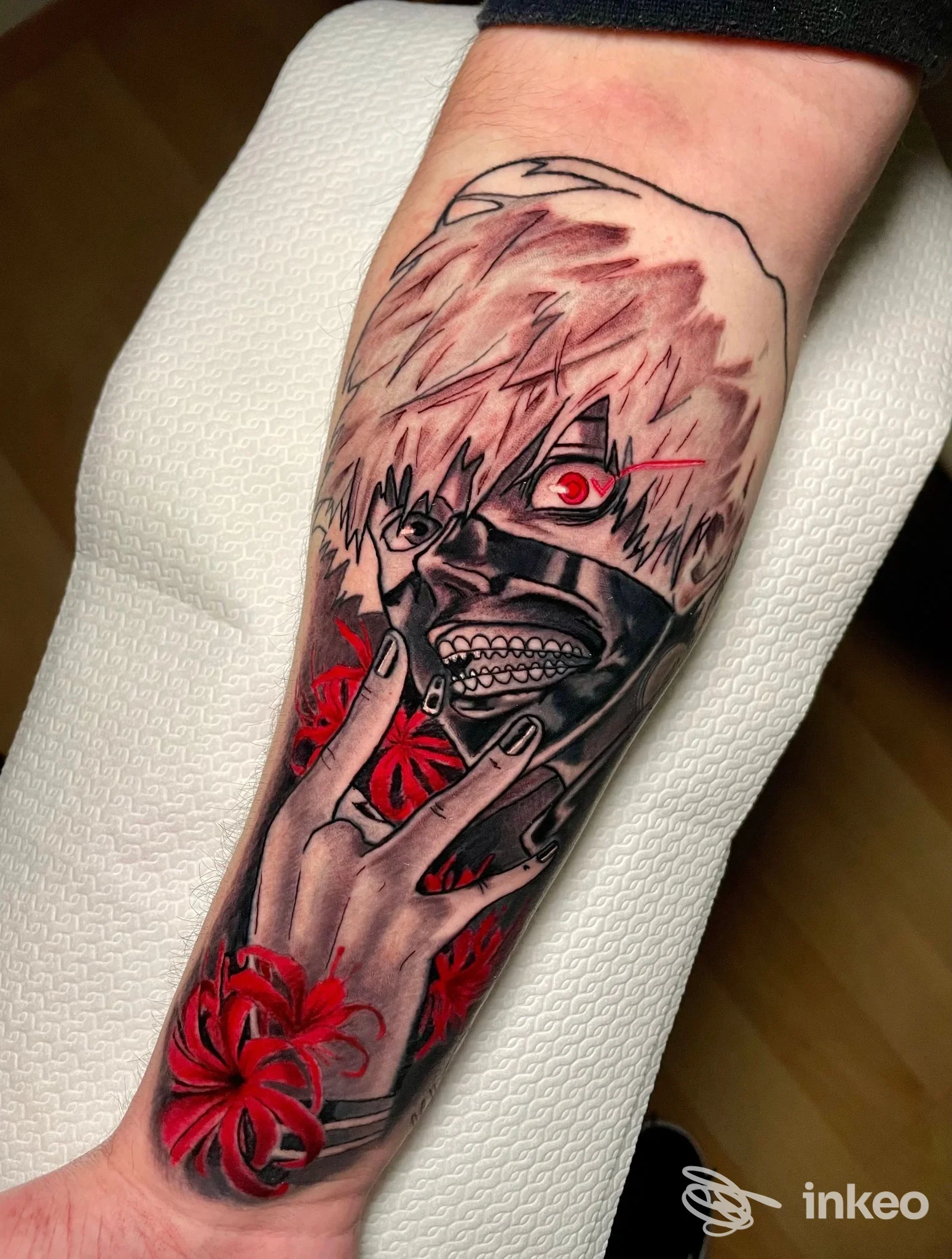 Tatuaggio in stile anime raffigurante volto mascherato e fiori rossi sull'avambraccio, foto fornita da Ink Tales Tattoo Studio, Gemona.