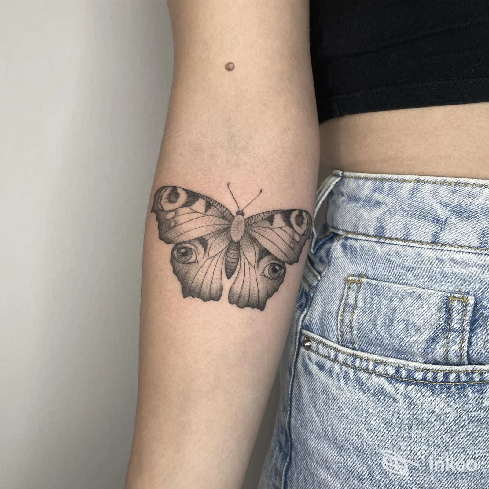 Farfalla tatuata in nero e grigio sull'avambraccio interno, scatto per Ink Blooms Tattoo Studio a Udine, dettagli lineari e ombreggiature sottili.