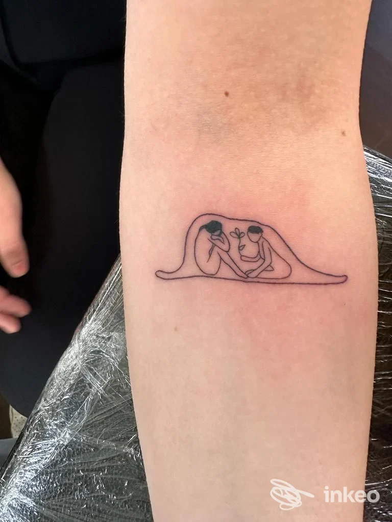 Tatuaggio lineare sull'avambraccio raffigurante due figure stilizzate sotto una coperta, Quincey Velvet Ink, Rivignano Teor.