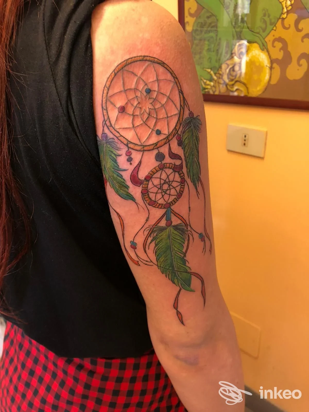 Tatuaggio acchiappasogni con piume verdi sul braccio superiore, foto fornita da Good Karma Tattoo, Trieste.