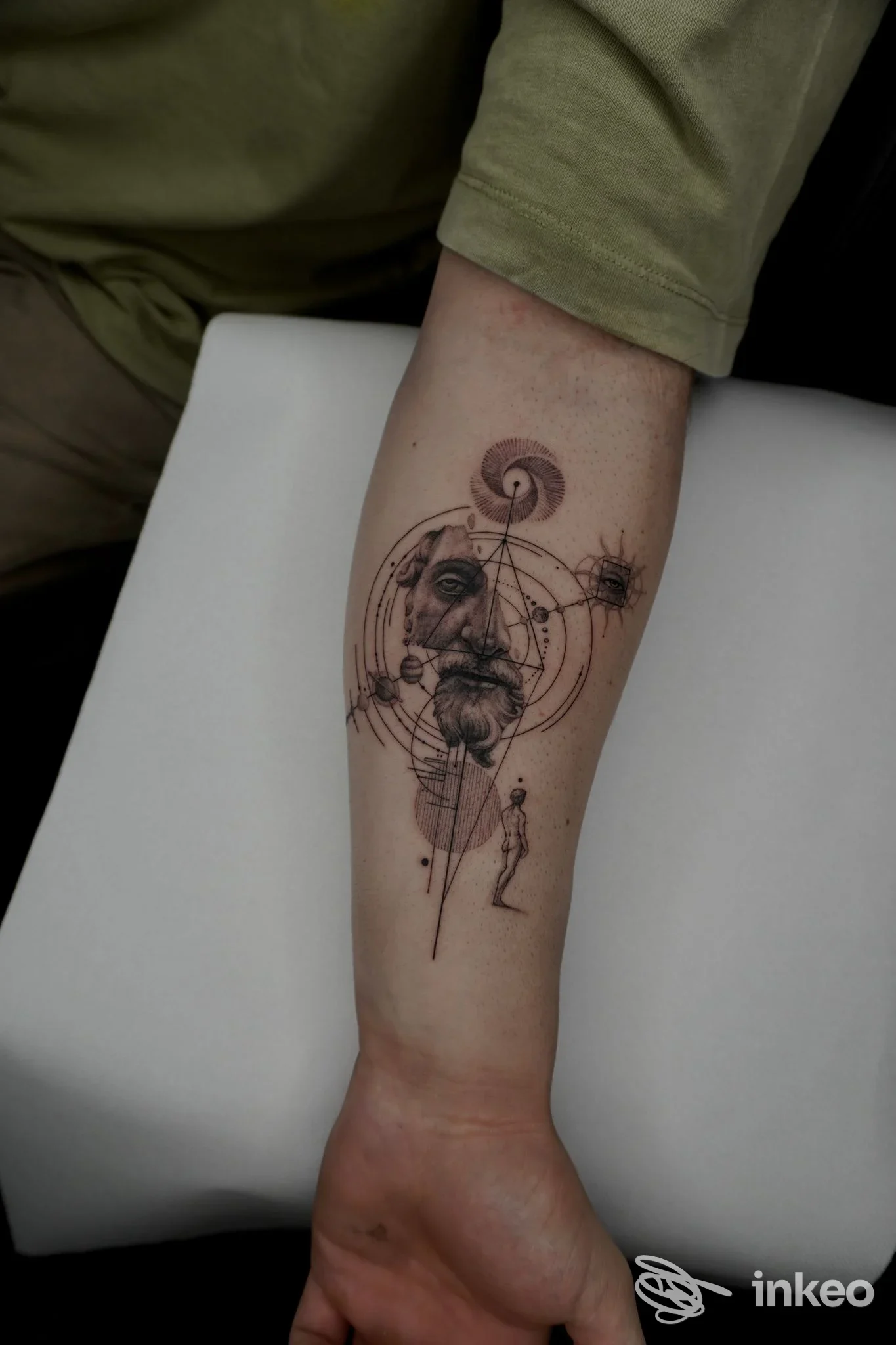 Tattoo sull’avambraccio raffigurante un volto stilizzato circondato da geometrie e simboli, eseguito da Berenice Tattoo; tatoo visibile su pelle reale.