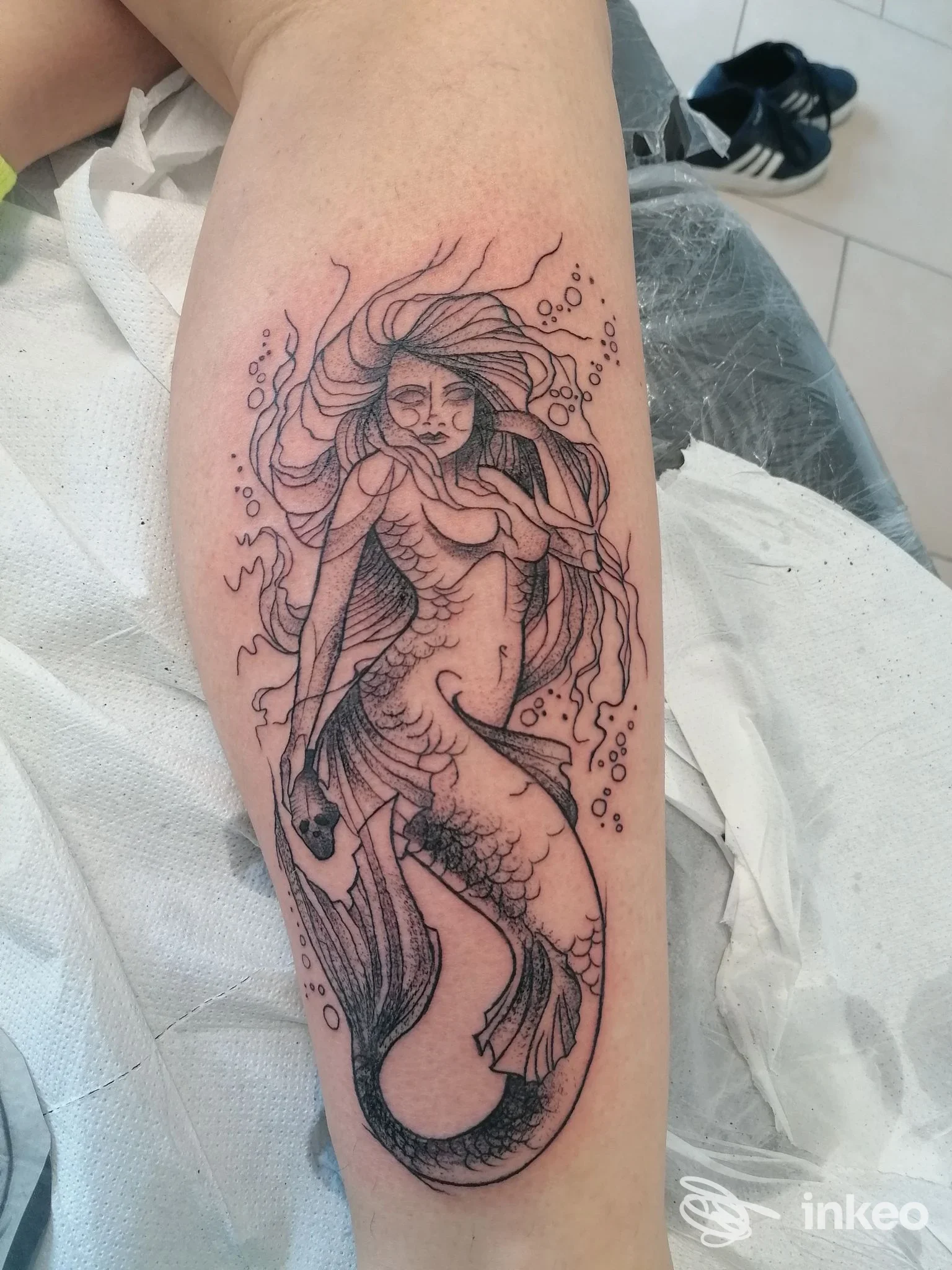 Tatuaggio sul polpaccio raffigurante una sirena in nero con linee sinuose e squame dettagliate, realizzato su pelle; Strega Ink Tattoo Studio, Villanova.