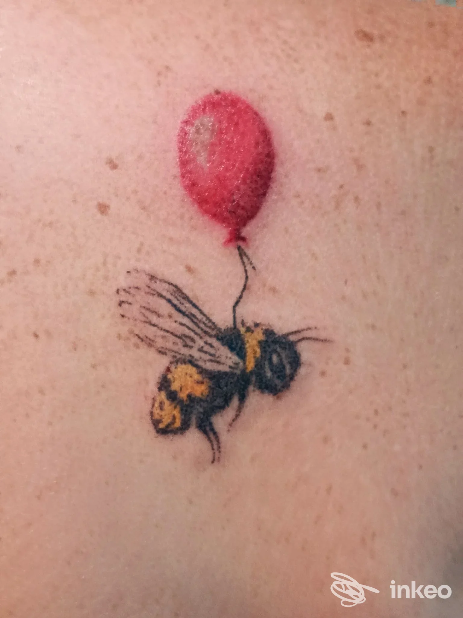 Piccolo tatuaggio handpoke di un'ape attaccata a un palloncino rosso su pelle chiara, realizzato da Ragnarok handpoke ritual tattoo studio a San Giovanni.