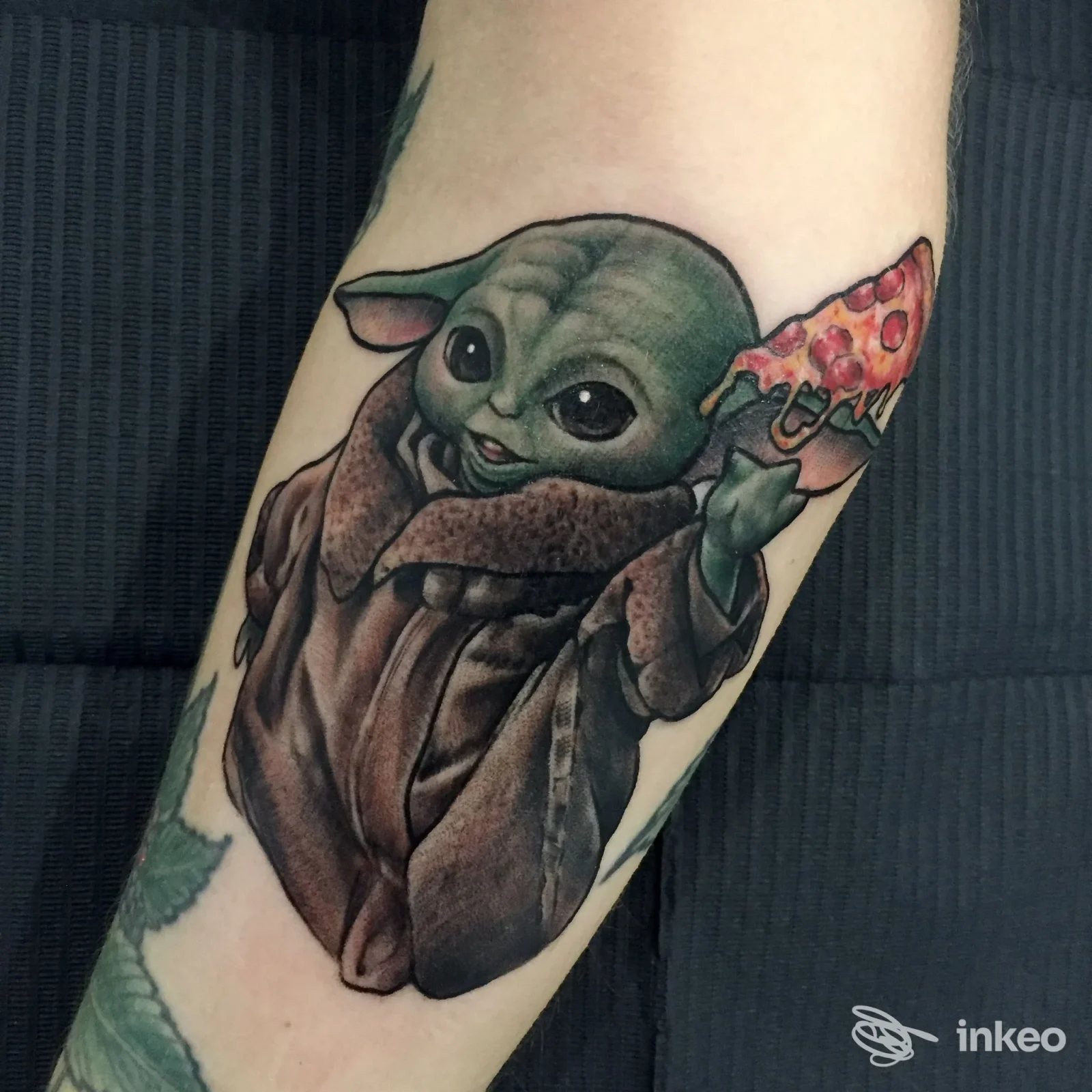 Tatuaggio a colori di Grogu con una fetta di pizza sull'avambraccio, realizzato da Obsidian Tattoo Atelier a Trieste.