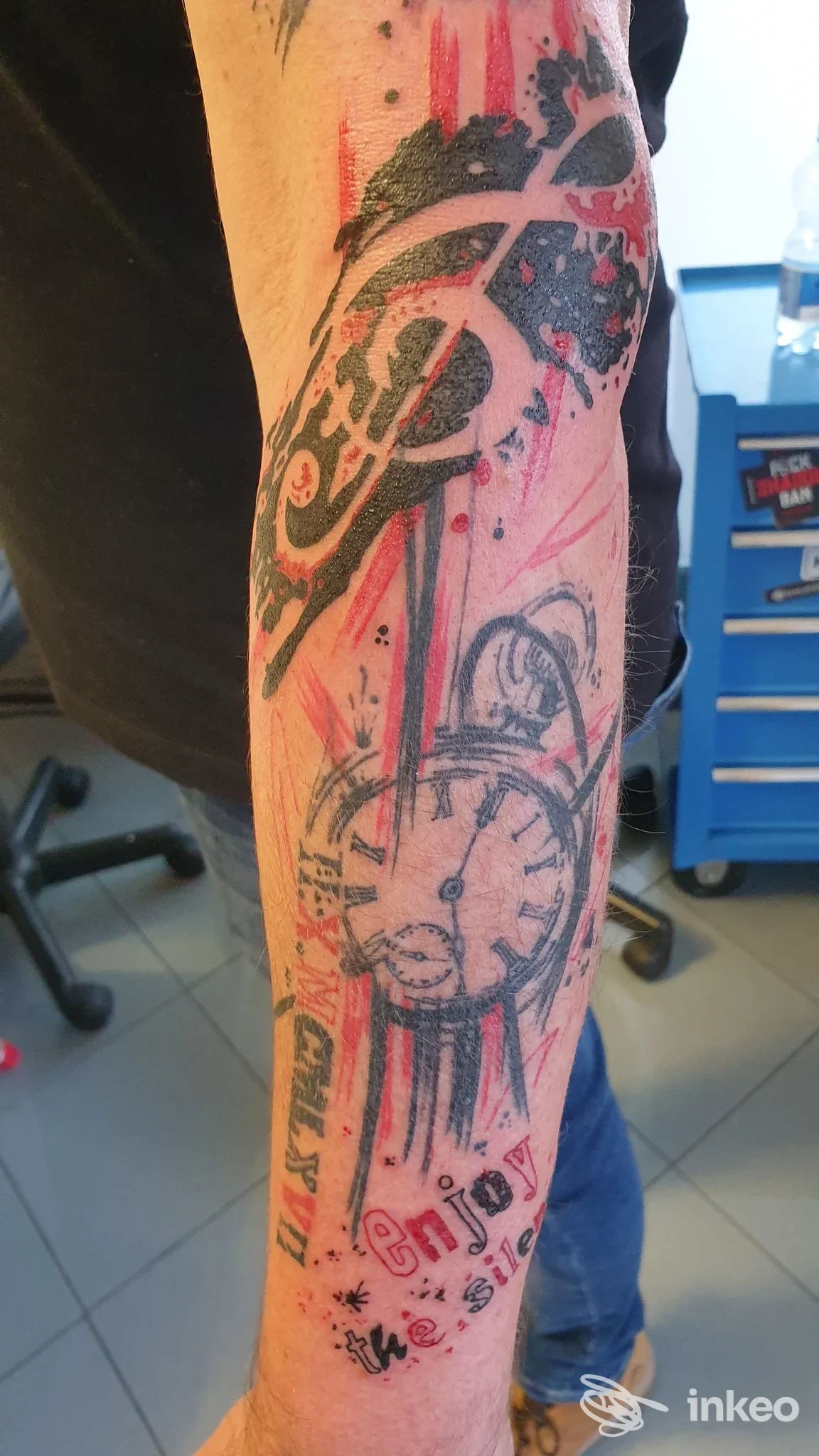 Tatuaggio esteso sull'avambraccio con orologio stilizzato e pennellate rosse, foto fornita da Tarzan Tattoo Studio, Pagnacco.