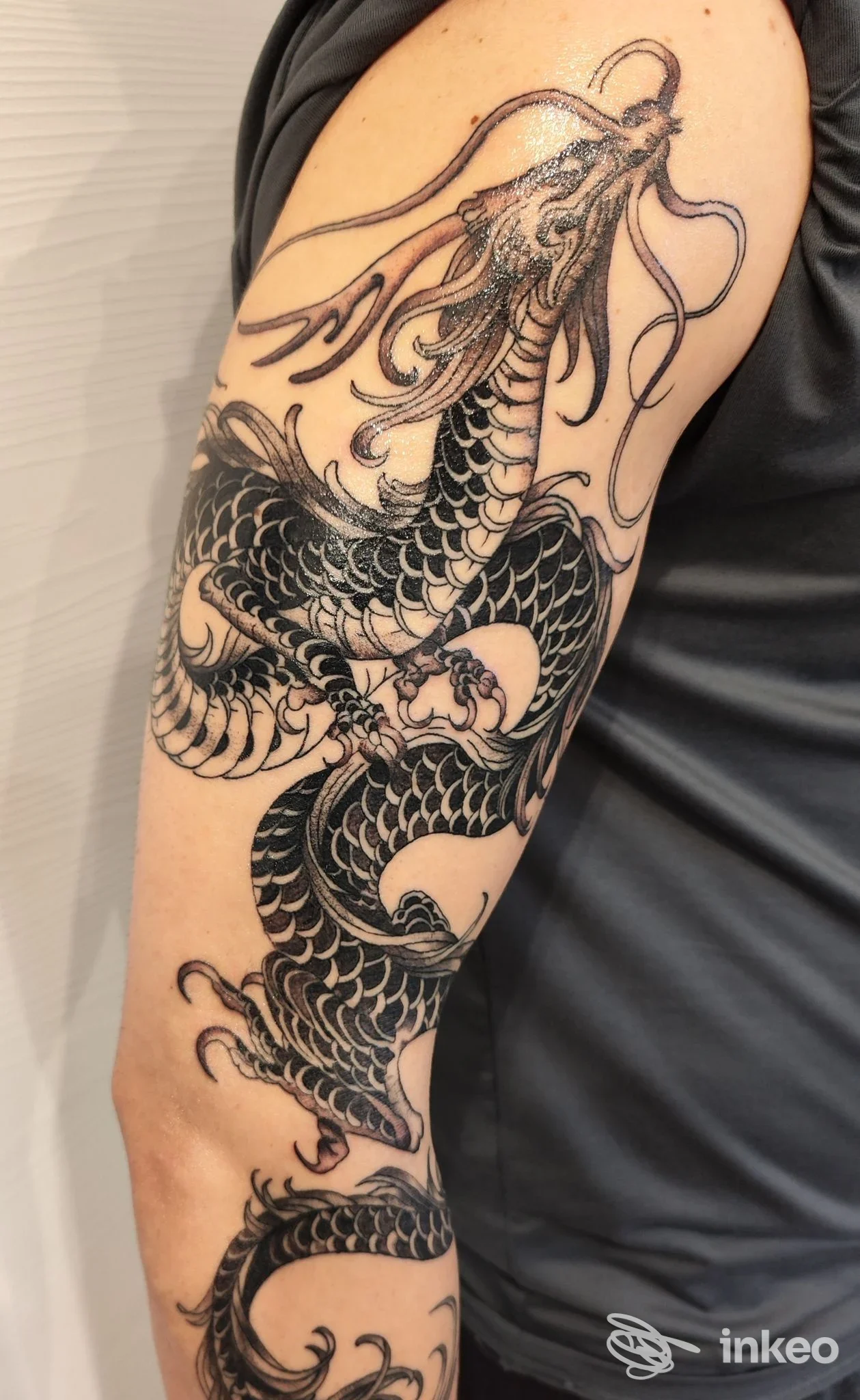 Tatuaggio a tema drago in nero avvolgente sul braccio, fotografia inviata dallo studio Marshall Tattoo a Pordenone.