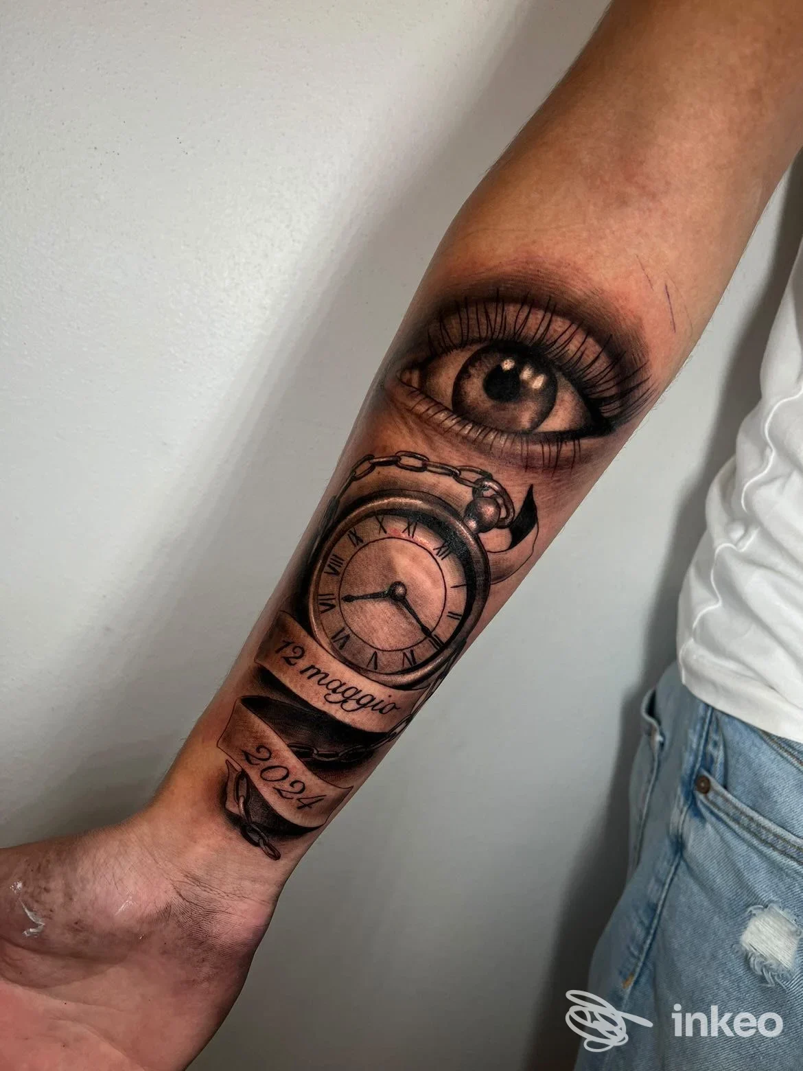 Tatuaggio realistico su avambraccio con un occhio dettagliato e un orologio da tasca; Pure Body Art, Trieste.