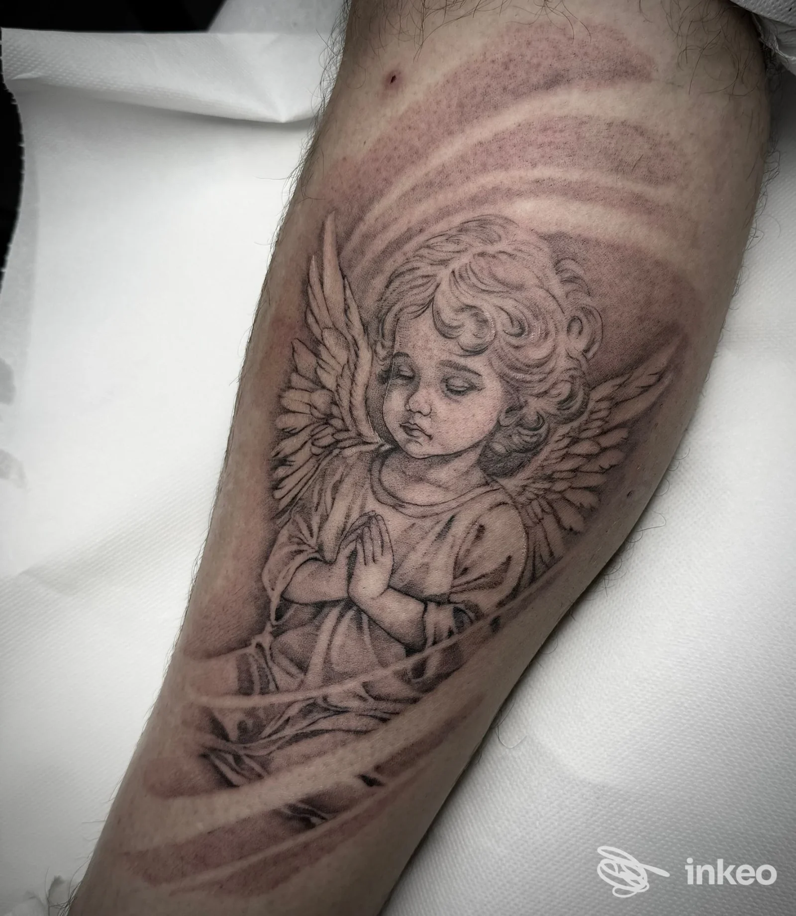Tatuaggio nero su polpaccio raffigurante un angelo bambino; lavoro pubblicato da LinfaNera a Latisana.
