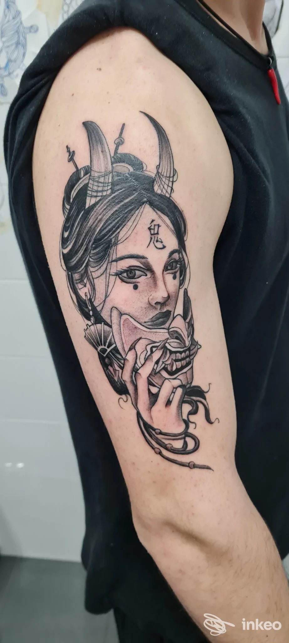 Tatuaggio in bianco e nero sul braccio superiore raffigurante volto femminile con maschera; realizzato da Solo Tattoo, Roma.