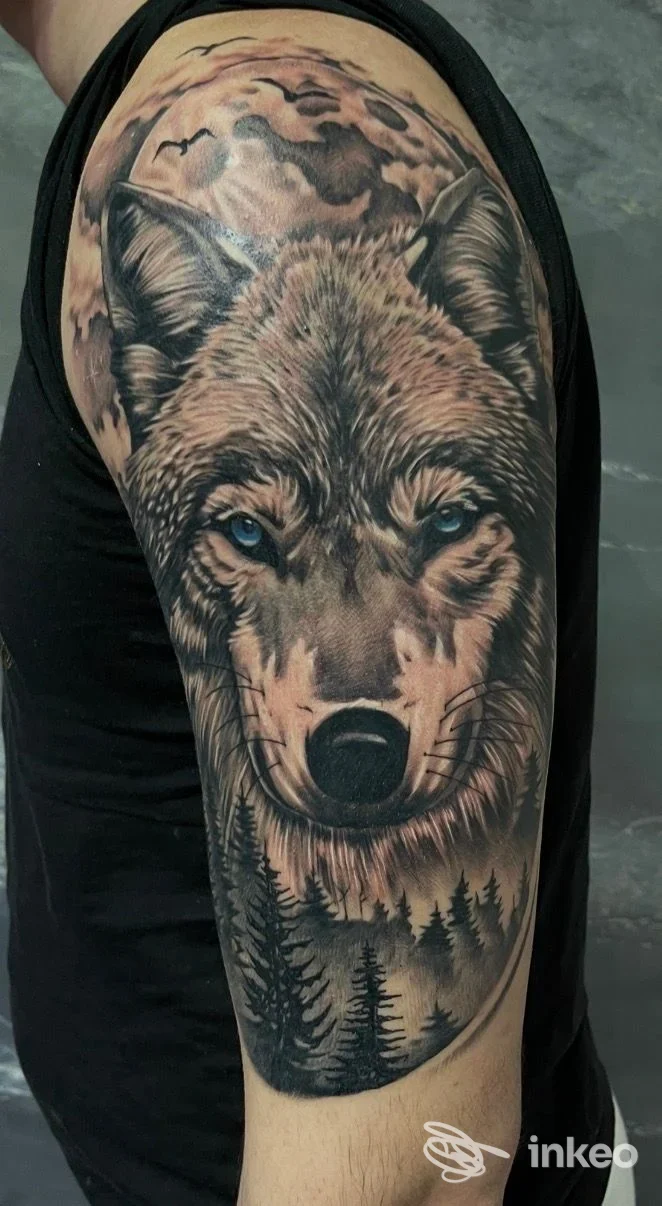 Grande tatuaggio realistico di un lupo sulla parte superiore del braccio, con foresta e cielo; Ago Matto Tattoo, Roma.