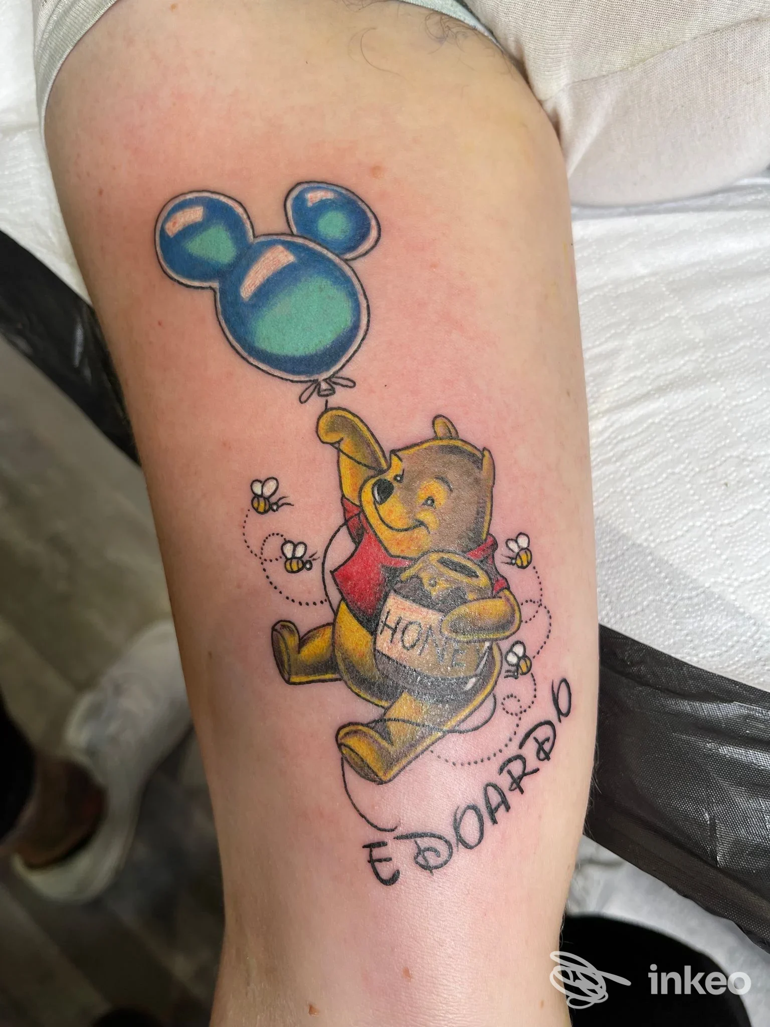 Tatuaggio cartoon di Winnie the Pooh con vasetto di miele e palloncino sulla coscia. Ago Matto Tattoo, Roma.
