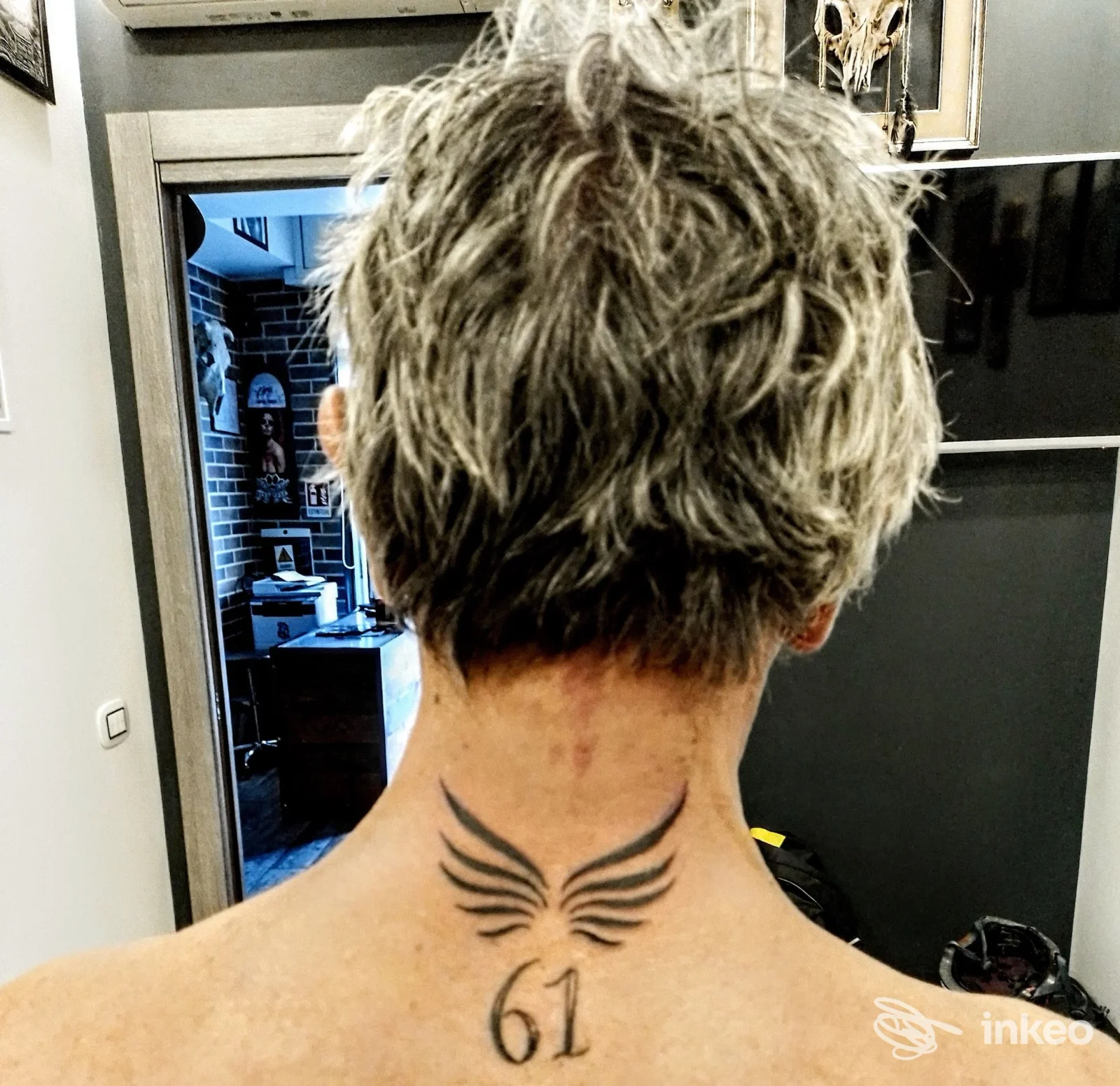Foto della nuca con tatuaggio al centro raffigurante ali stilizzate e il numero '61', scattata presso Airis Tattoo a Roma.