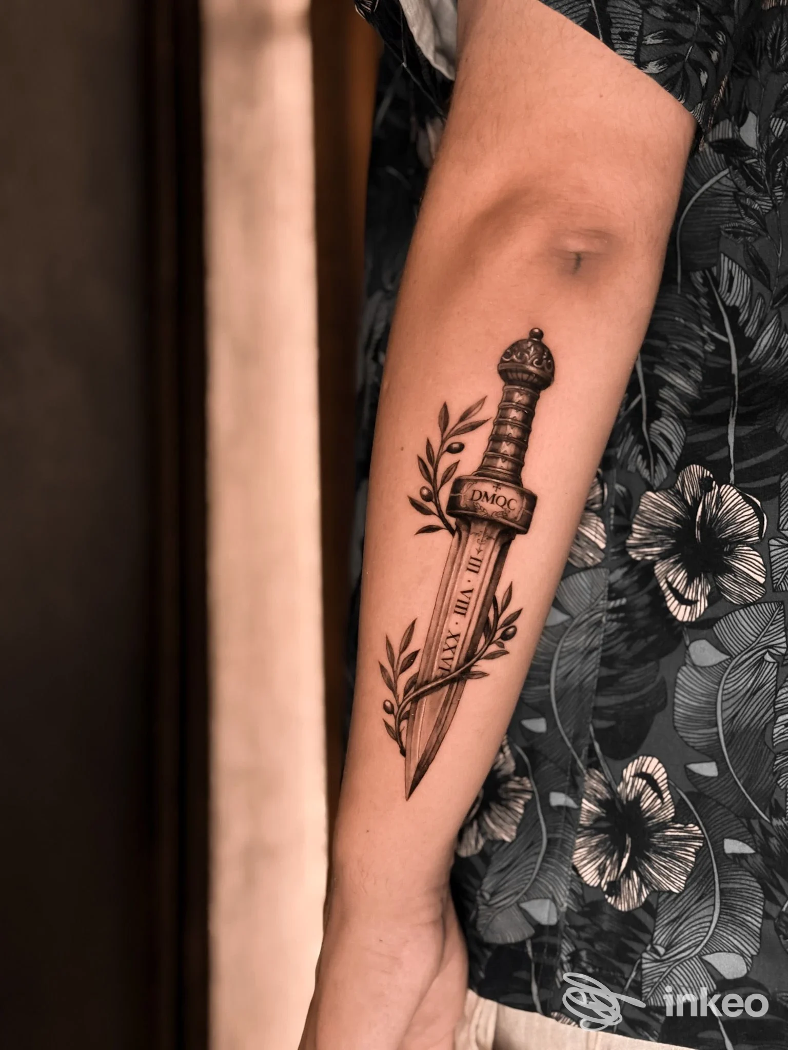Primo piano dell'avambraccio con tatuaggio a pugnale e rami in bianco e nero, scatto verticale — Aureo Roma Tattoo & Gallery, Roma.