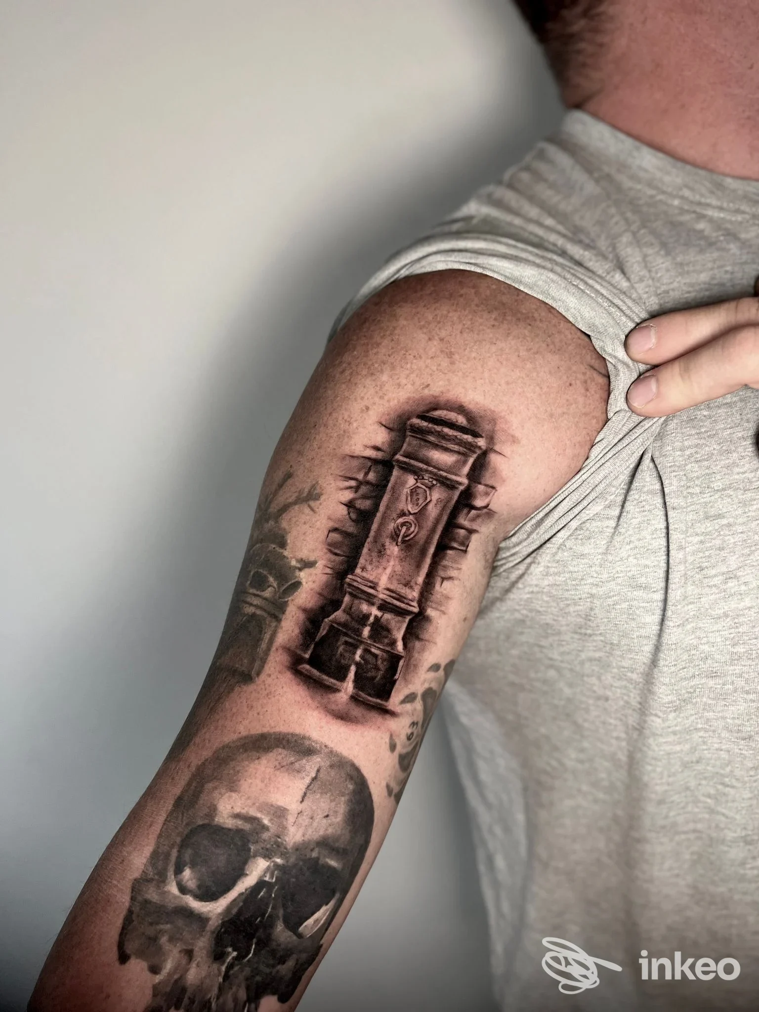 Braccio con tatuaggi realistici in bianco e nero: colonna stilizzata sulla spalla e teschio sull'avambraccio. AVVERSO TATTOO, Roma.