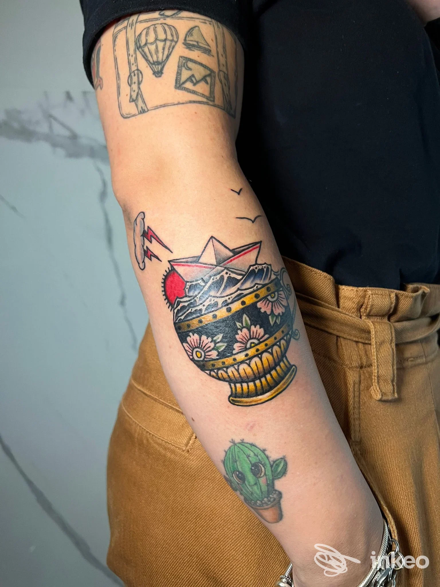 Avambraccio tatuato con vaso decorativo e piccoli soggetti floreali, foto inviata da AVVERSO TATTOO Roma.
