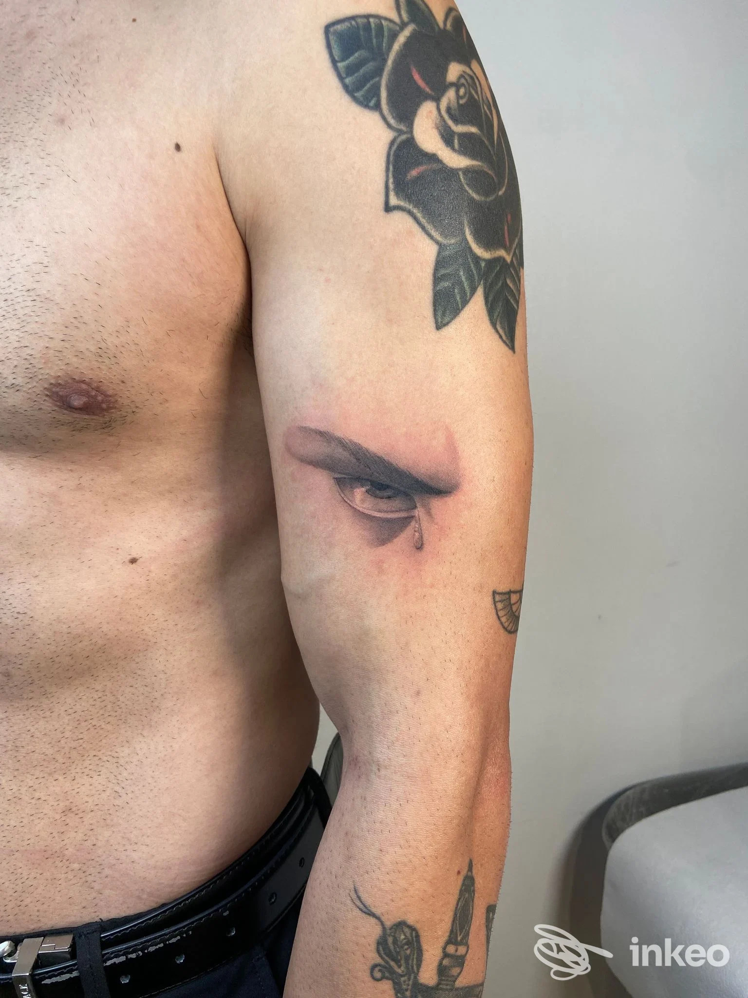 Dettaglio di tatuaggi su spalla e braccio con occhio realistico e rosa, fotografia di BAGHERA Tattoo Studio a Ceccano.