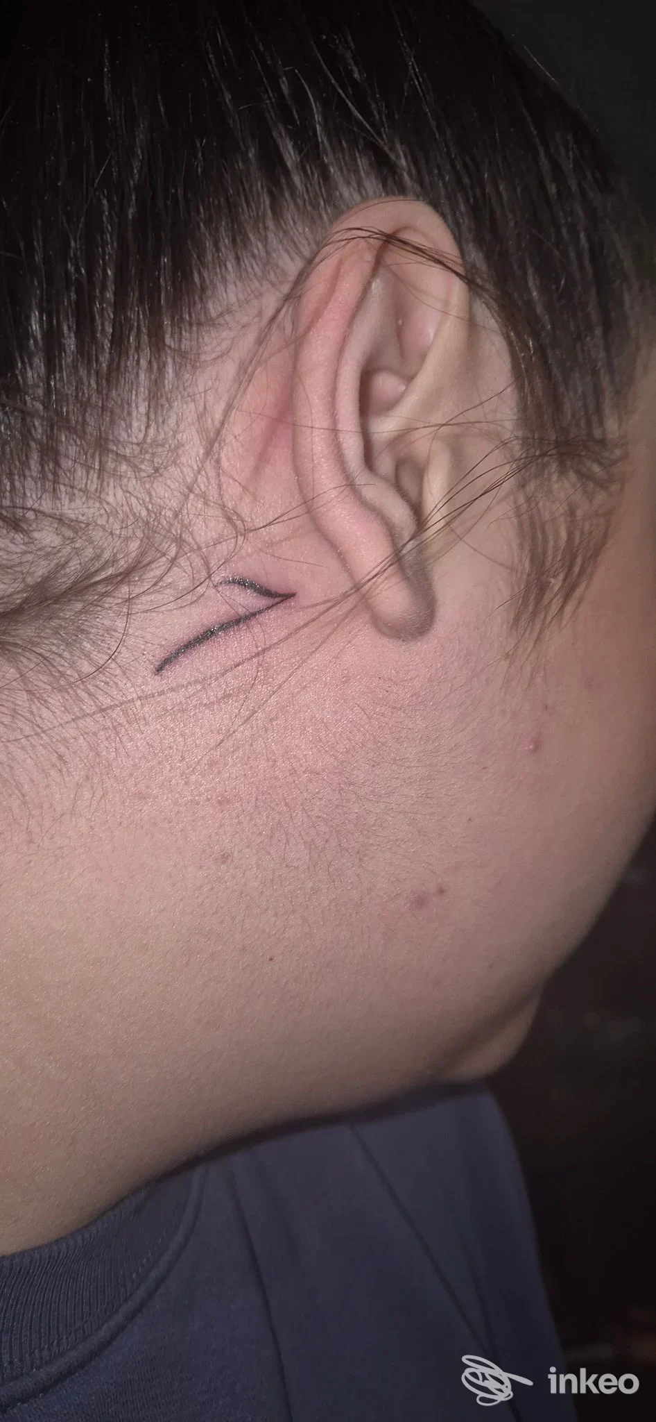 Primo piano di un piccolo tatuaggio a due linee nere vicino all'orecchio. Black Rose Tattoo Studio, Sora.