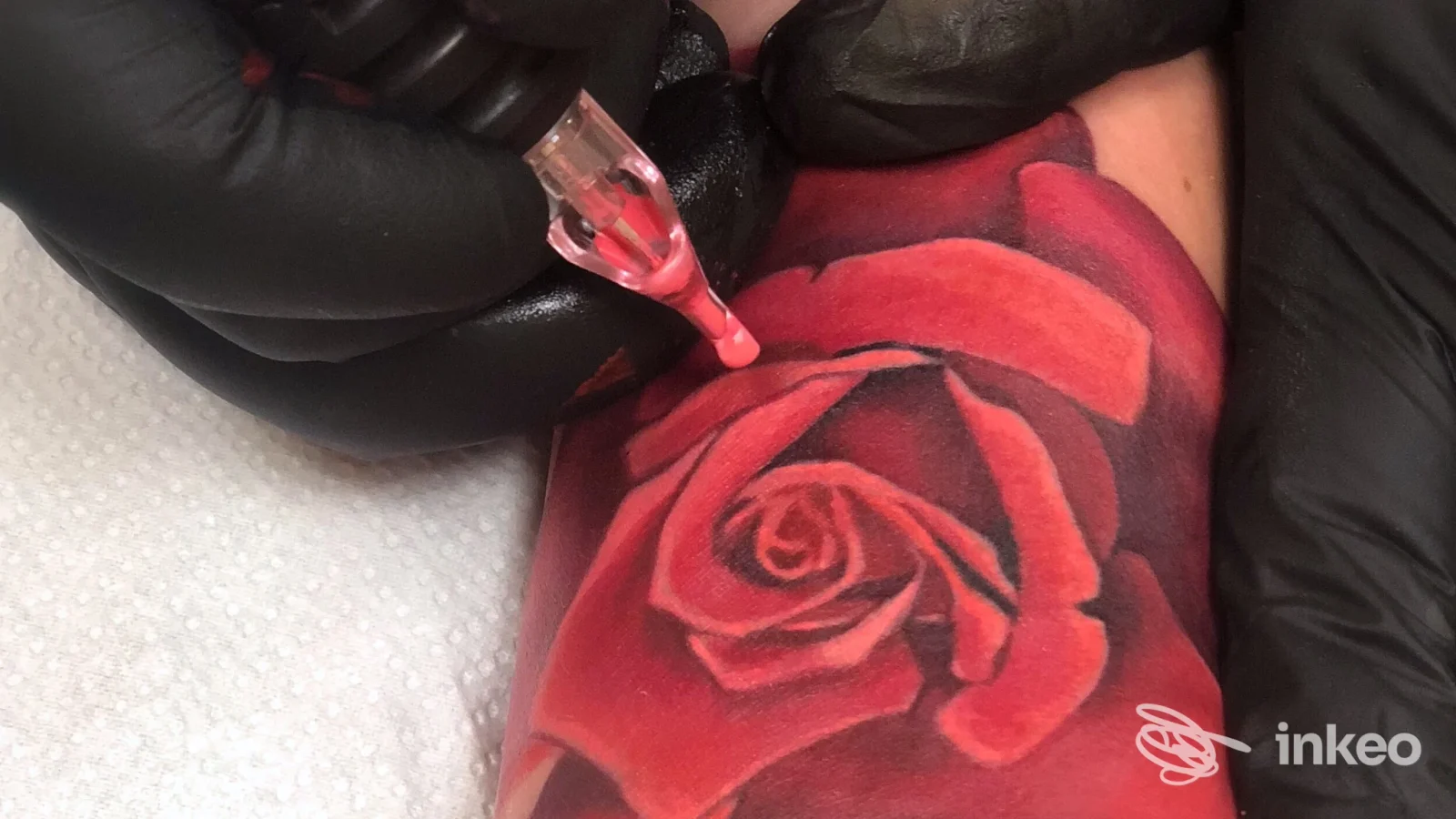 Primo piano di una rosa tatuata in corso sull'avambraccio, mani guantate e macchinetta visibili. Blood Colour Tattoo Studio, San Cesareo.