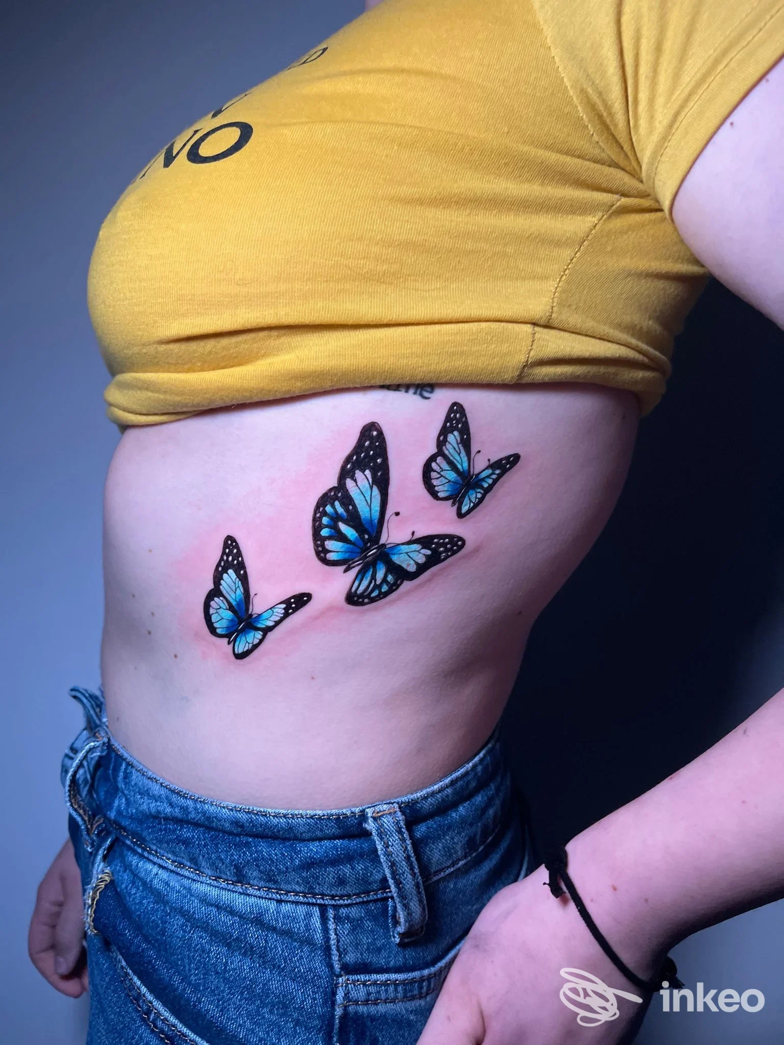Tre farfalle blu tatuate sul fianco di una persona in primo piano; lavoro di CRIMSON BLOOD tattoo studio, Roma.