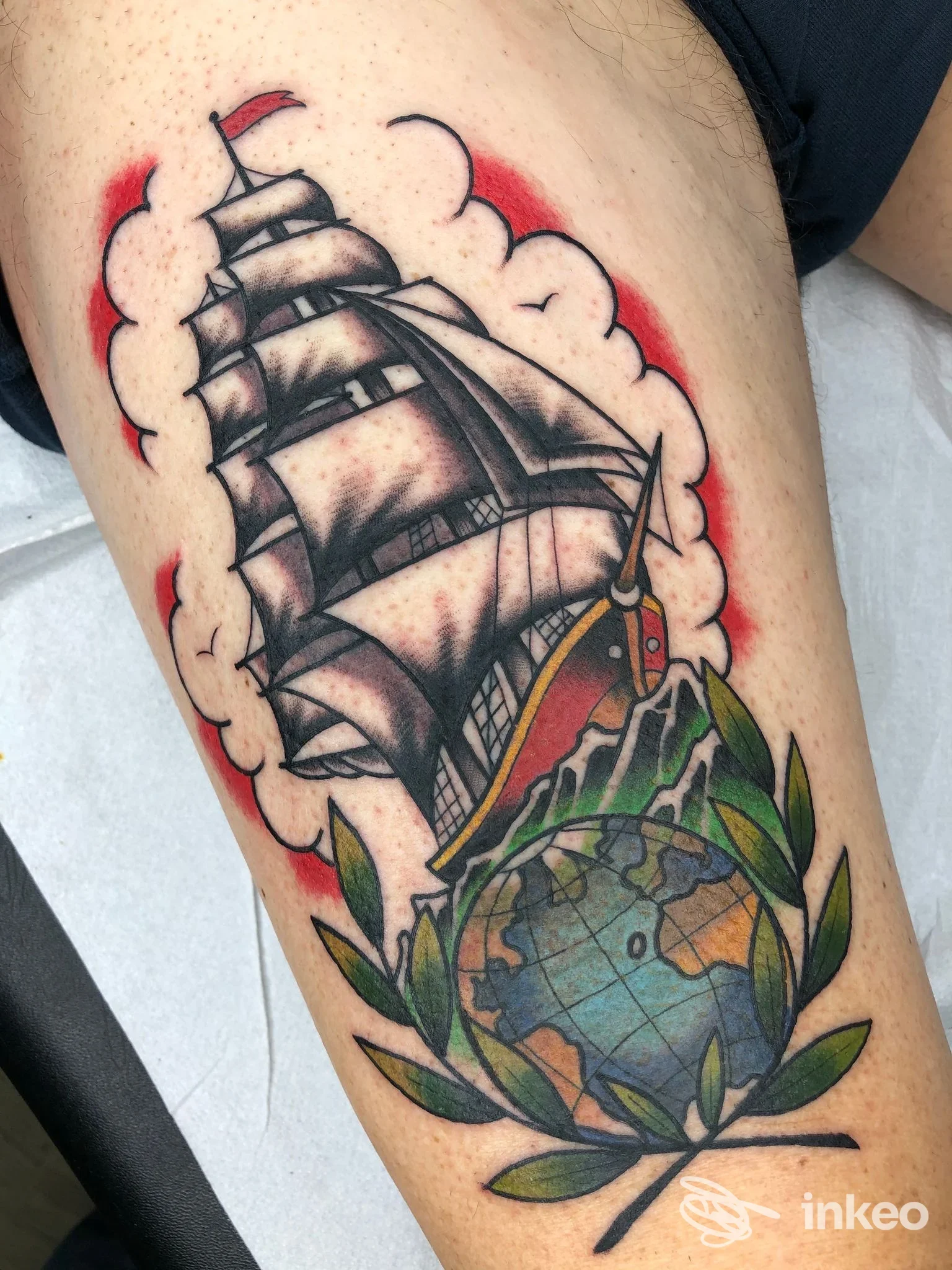 Tatuaggio su coscia raffigurante una nave a vele sopra un mappamondo con foglie, foto fornita da Dear John Tattoo, Velletri.