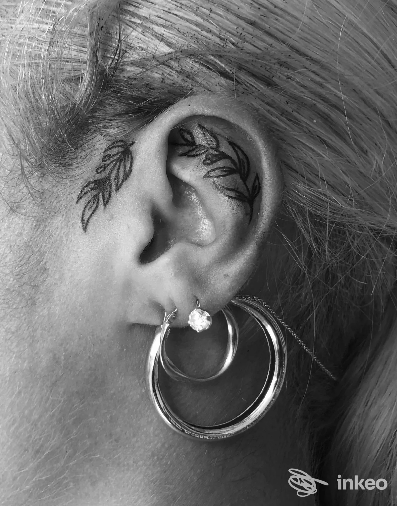 Primo piano di un orecchio tatuato con motivo a foglie realizzato da Devil's Mind Tattoo a Passoscuro, con orecchino a cerchio.
