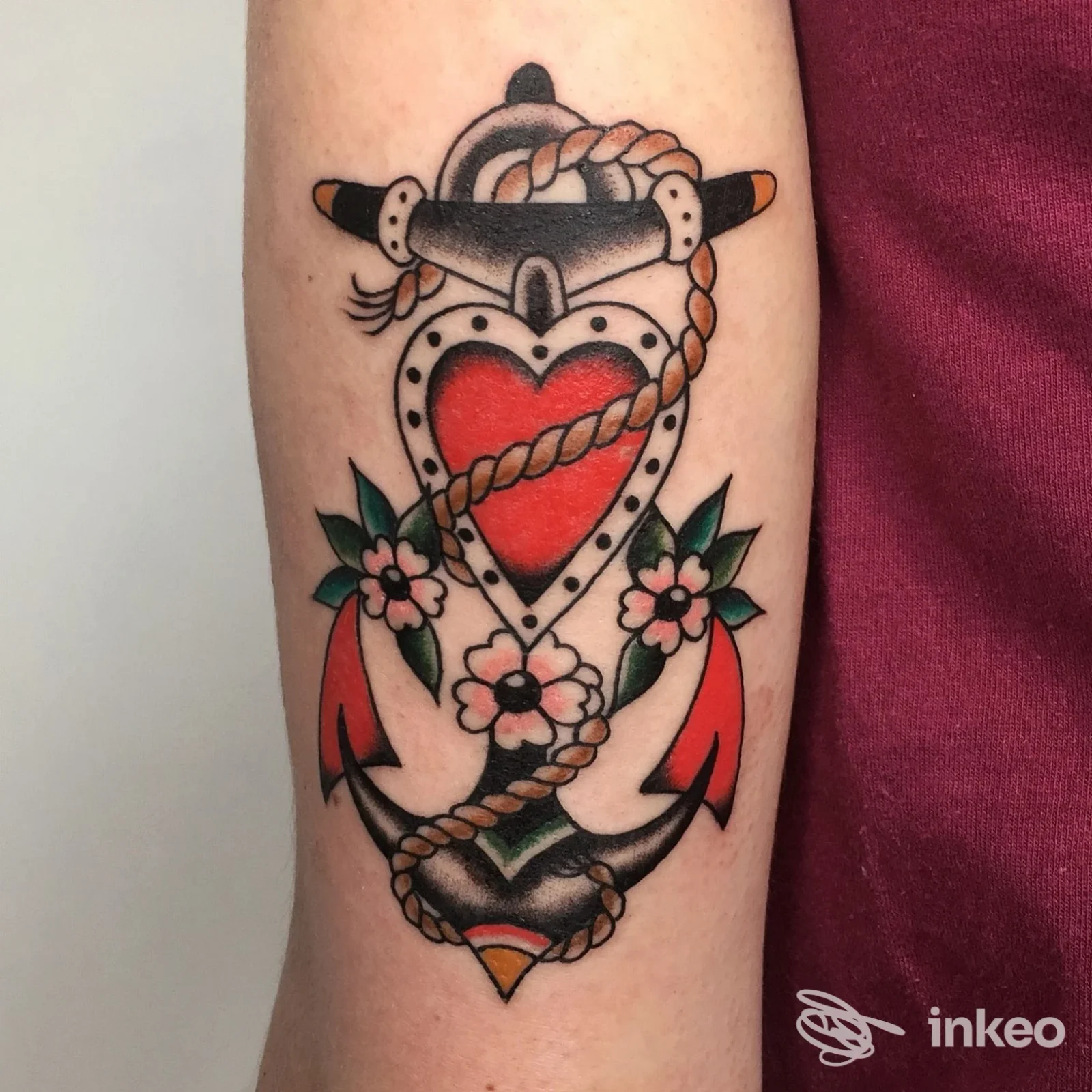 Fotografia ravvicinata di un tatuaggio in stile traditional con ancora, cuore e fiori sull'avambraccio, eseguito da Electric Wizard Tattoo a Roma.