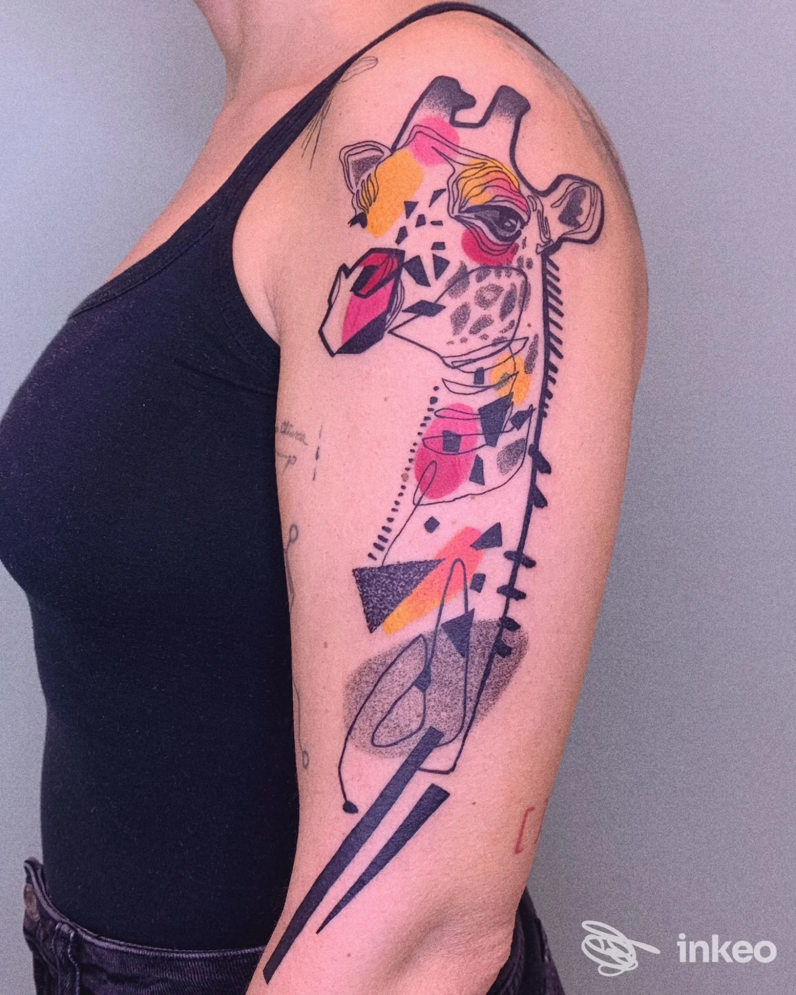 Tatuaggio colorato a tema giraffa sul deltoide e braccio superiore, fotografia di Elena Fortuna Tattoo a Roma che mostra linee geometriche e colori vivaci.