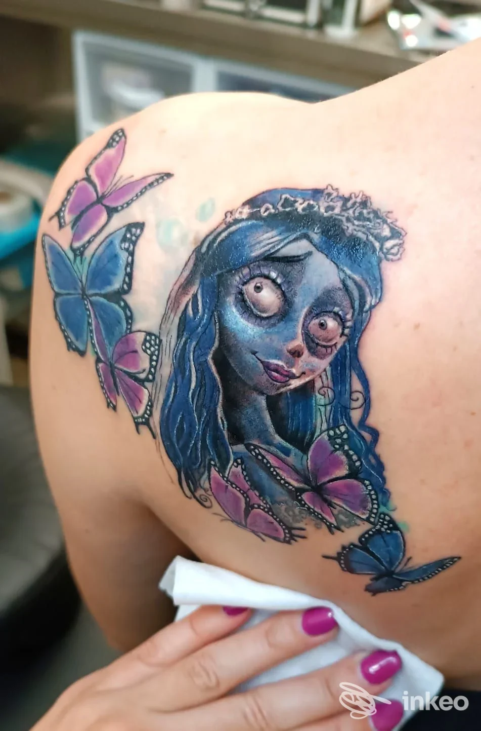 Tatuaggio su spalla con ritratto stilizzato blu e farfalle viola, realizzato da Emme Erre Tattoo Factory, Vetralla.