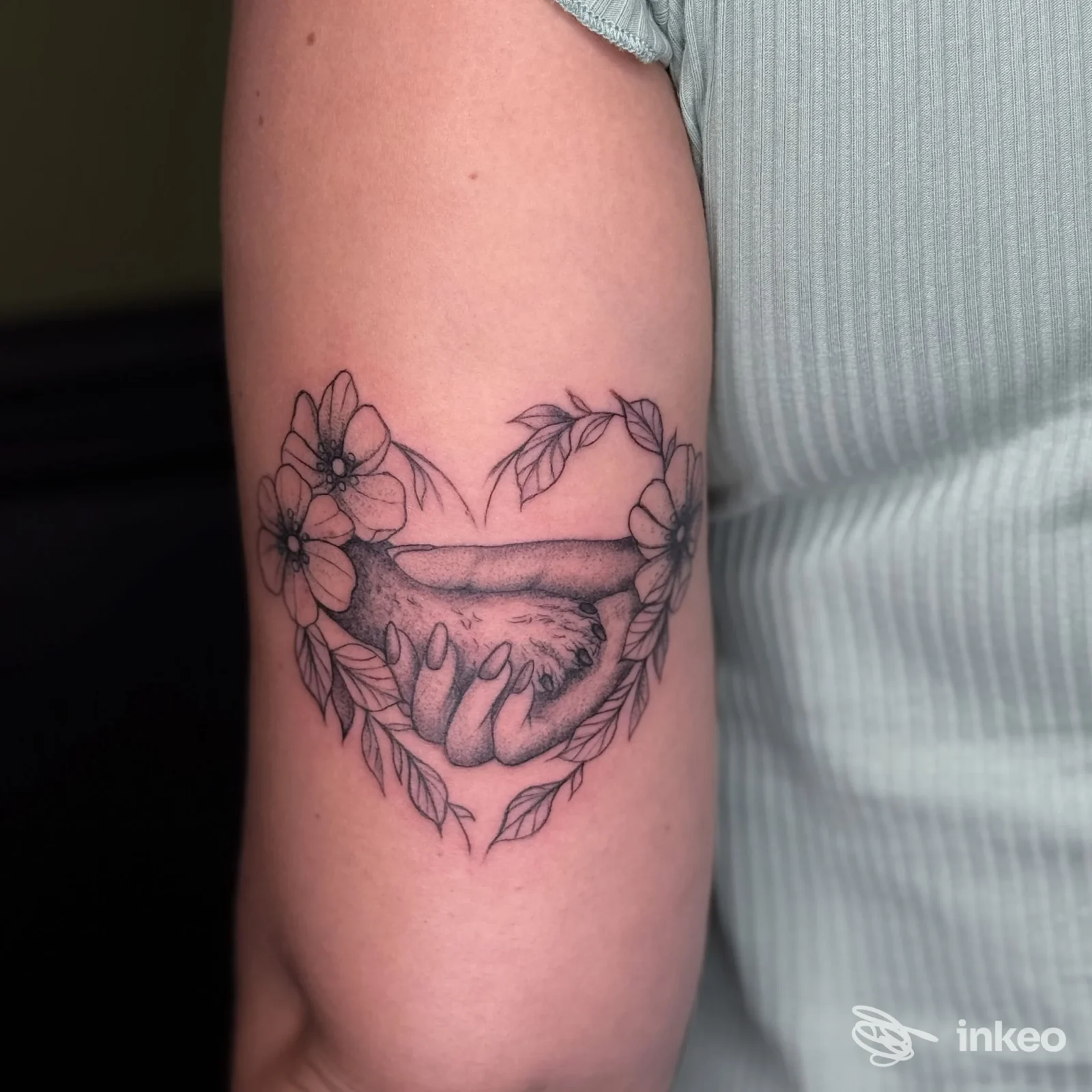 Tatuaggio a inchiostro nero di due mani che si stringono circondate da fiori sul tricipite, Elisabeth Consoli Tattoo Artist, Latina.