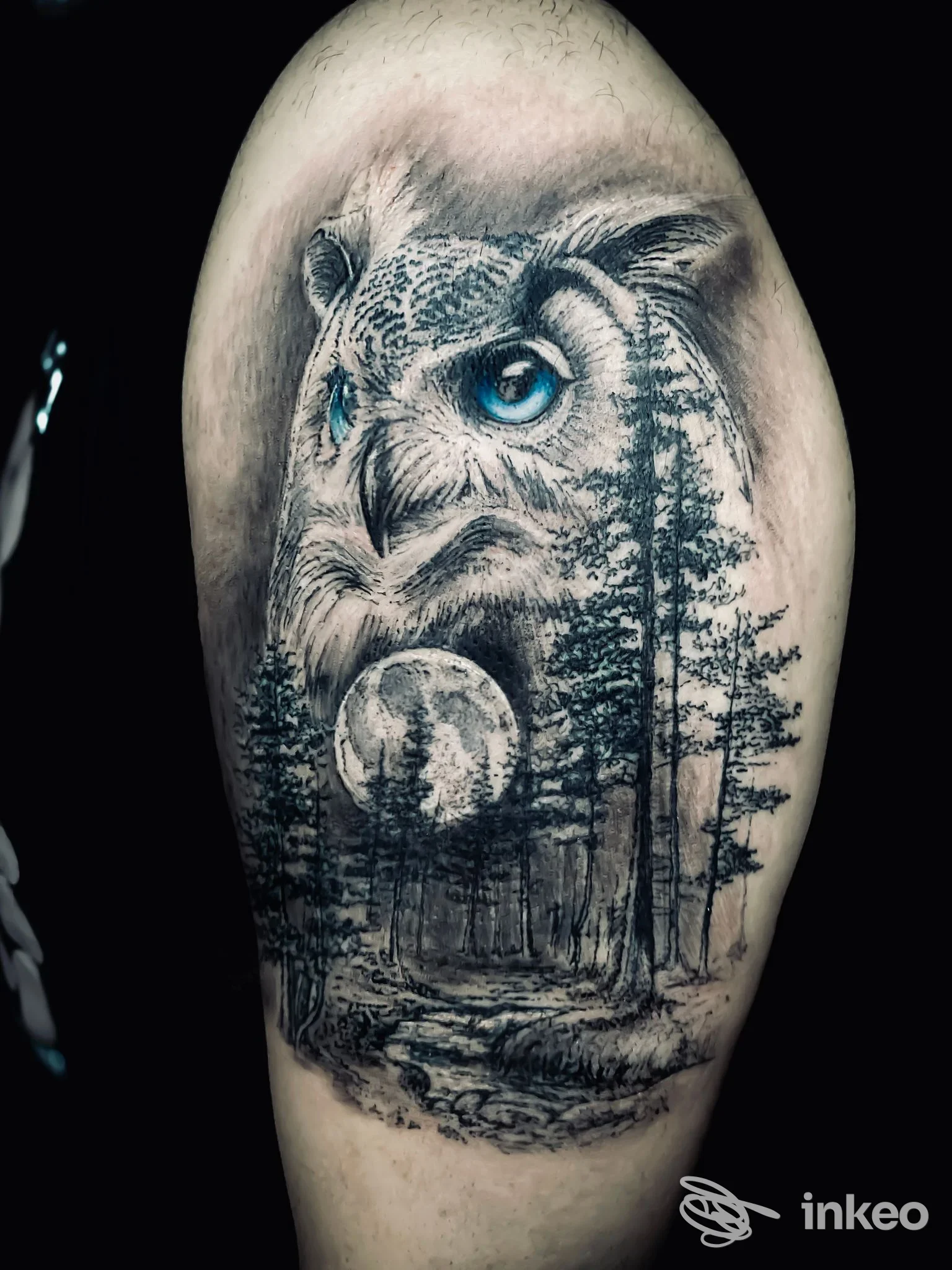 Grande tatuaggio realistico di un gufo con occhi blu e paesaggio boschivo sull'esterno del braccio, Enrico Marconi Tattoo, Roma.
