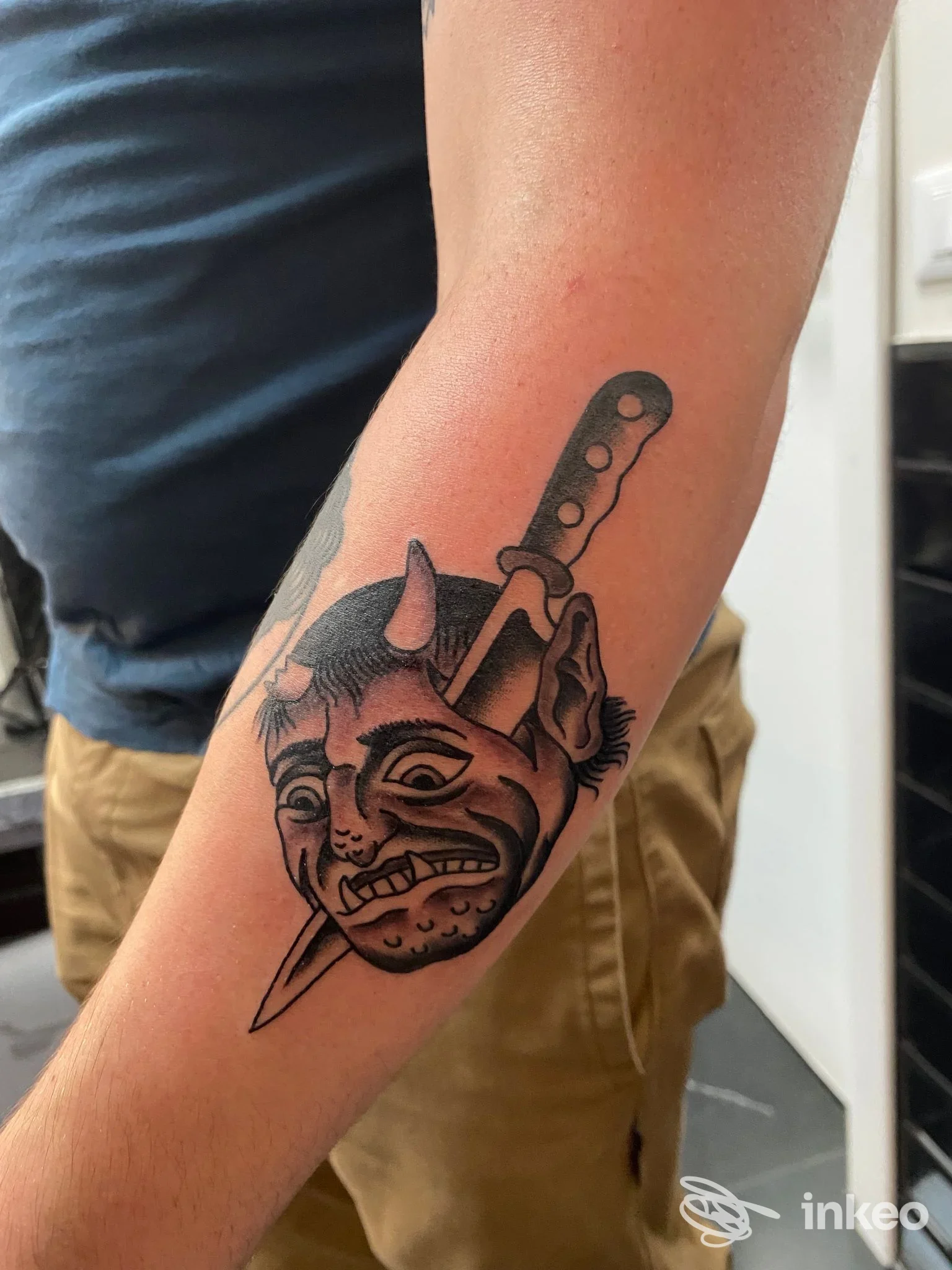 Tatuaggio su avambraccio con volto demoniaco trafitto da un coltello, scatto interno. Eternal City Tattoo - Roma.