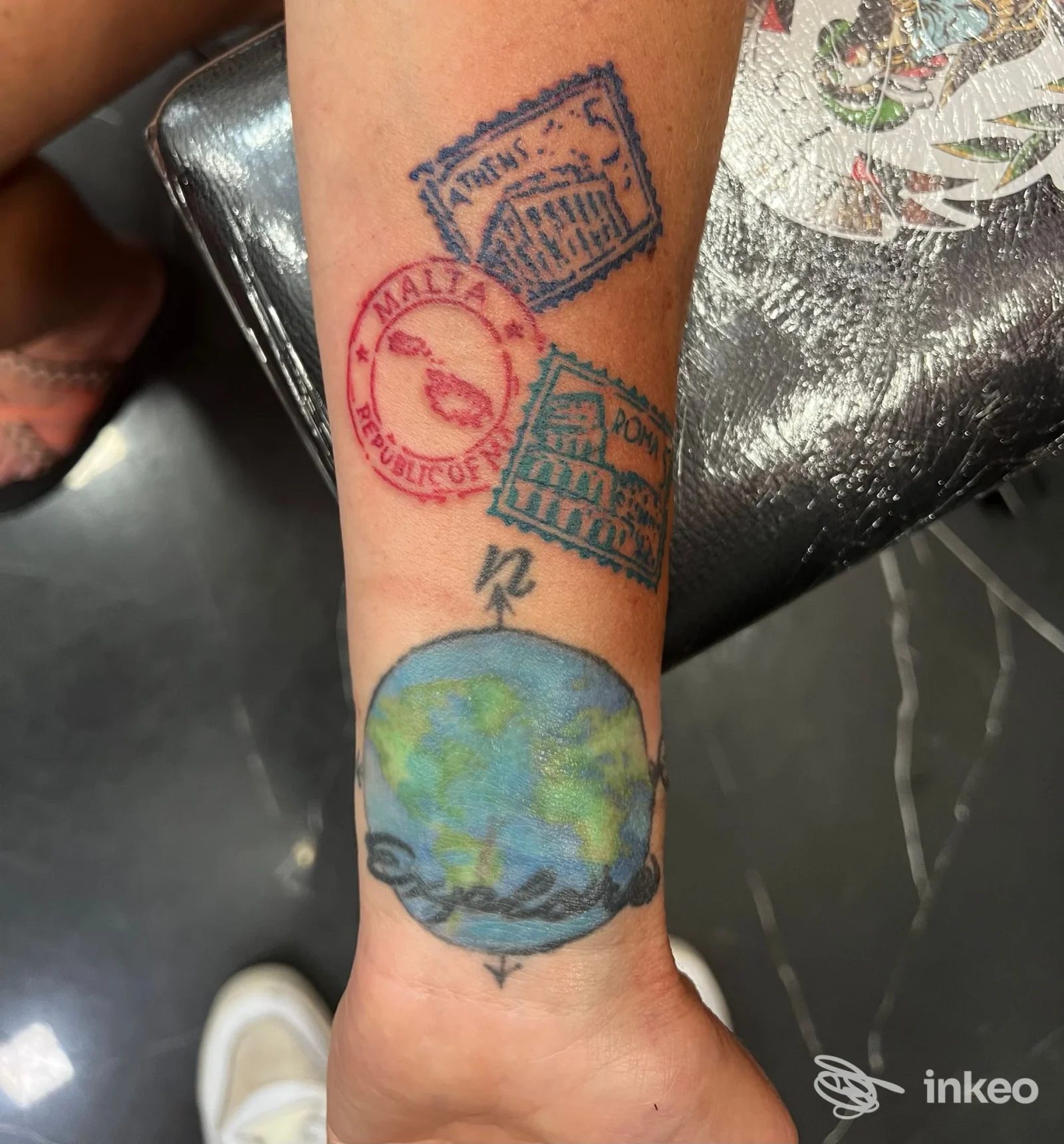 Avambraccio tatuato con timbri colorati e un mappamondo; Eternal City Tattoo - Roma mostra lavoro a colori sul polso.