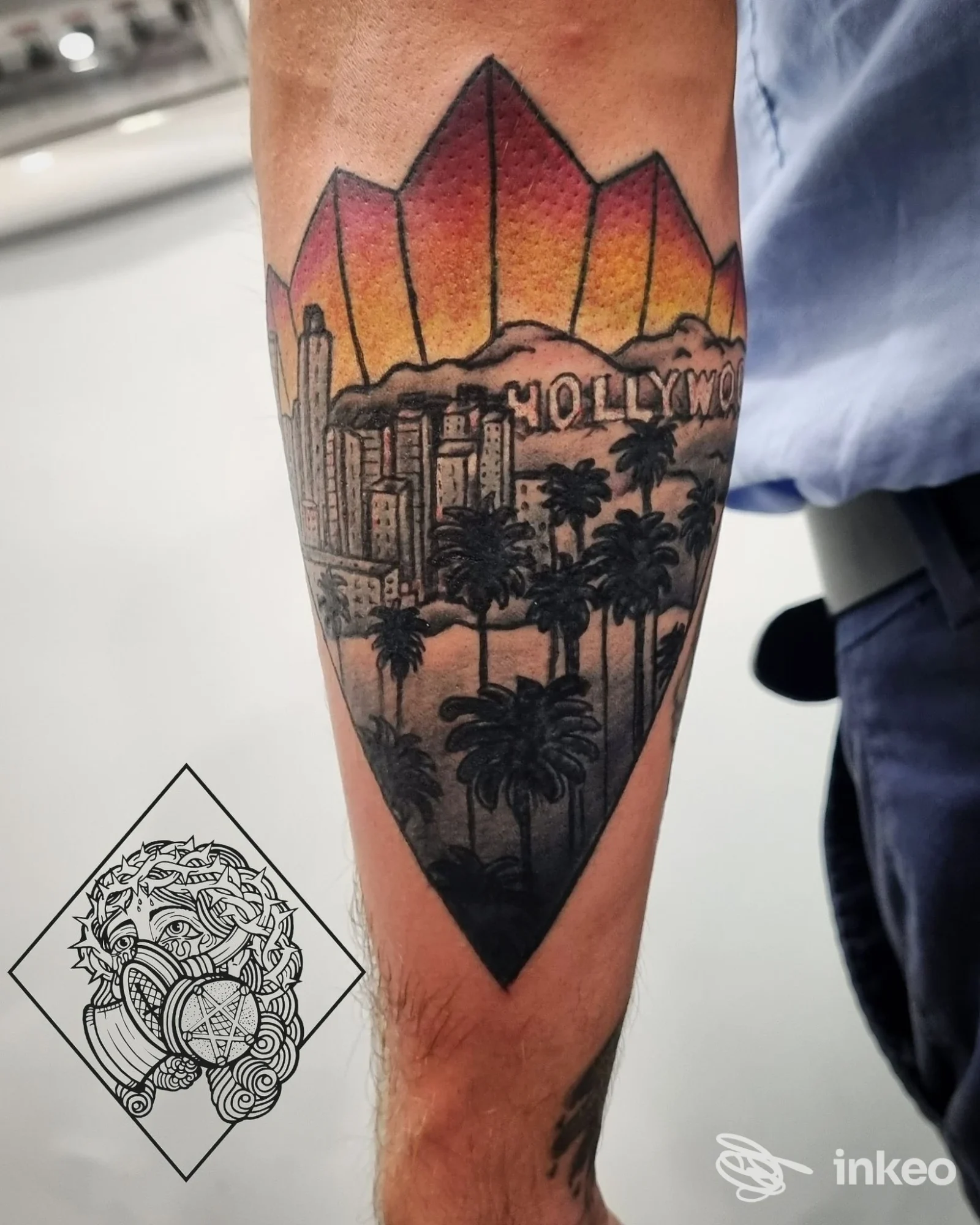 Tatuaggio a scudo con skyline e palme sull'avambraccio, colori caldi e dettagli in nero — Family Tattoo Shop, Roma.
