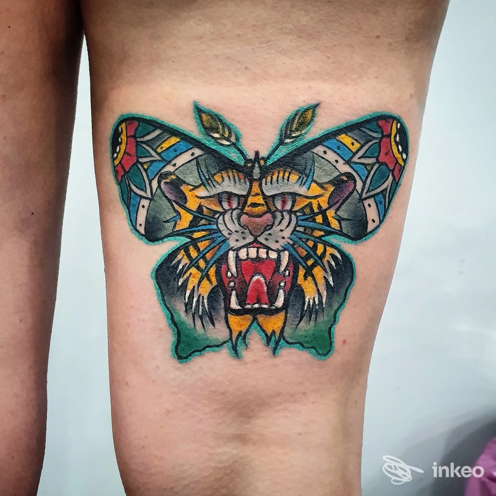 Tatuaggio a colori che combina una tigre stilizzata e ali a forma di farfalla sulla parte alta della coscia, eseguito da Family Tattoo Shop a Roma, linee nette e colori vividi.