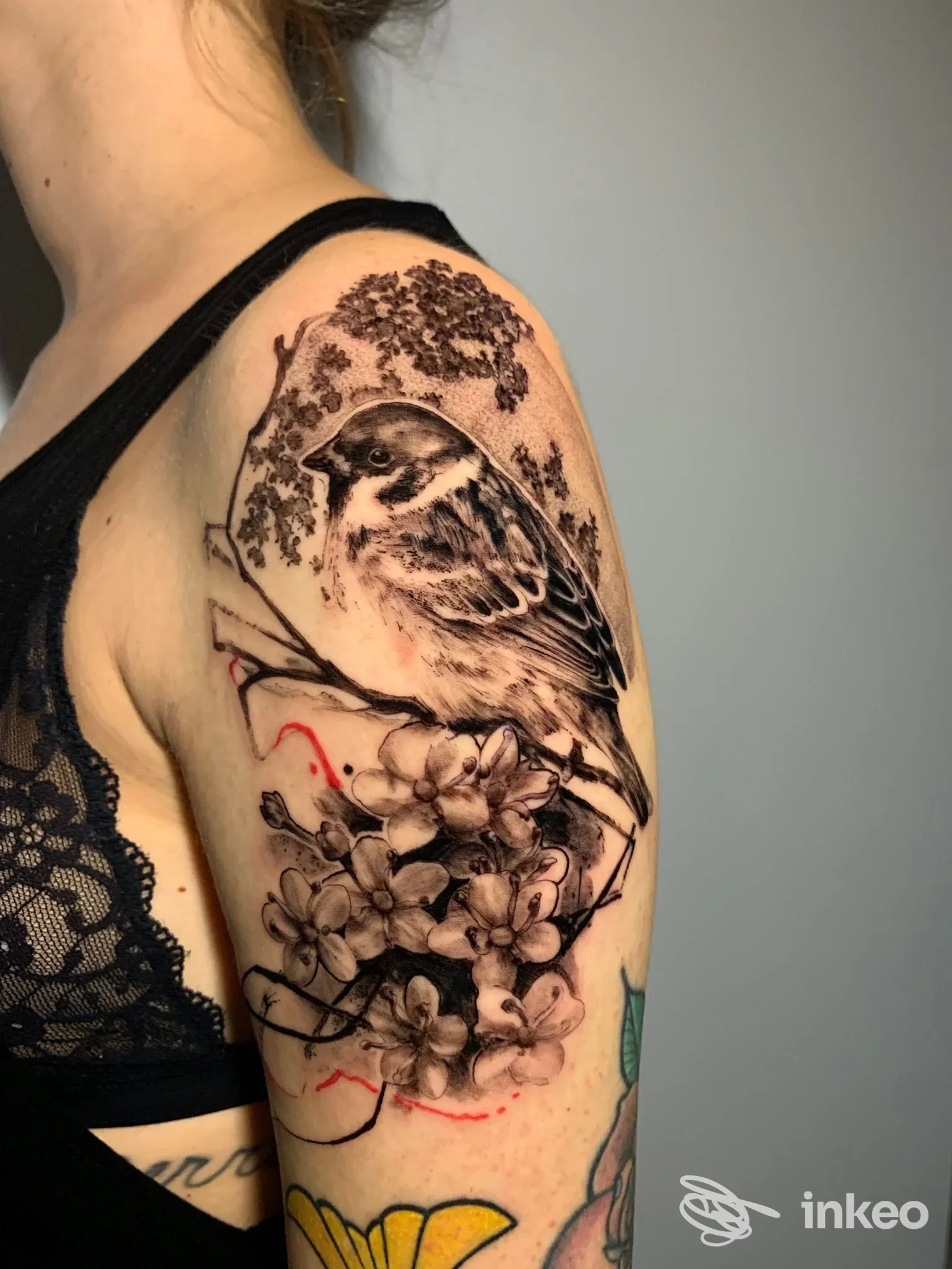 Tatuaggio realistico di uccello con fiori sulla spalla e braccio superiore, foto dello studio Greyhounds tattoo, Roma.