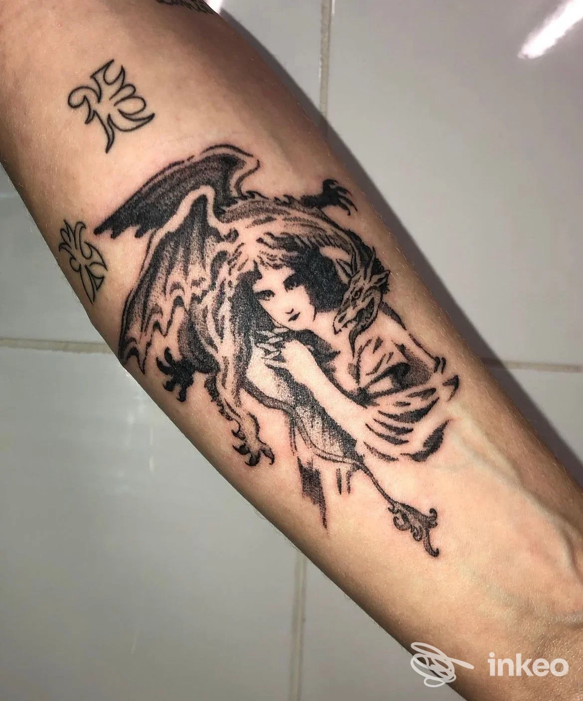 Tatuaggio in bianco e nero su avambraccio che raffigura una figura alata; immagine fornita da Hard Work Tattoo, Roma.