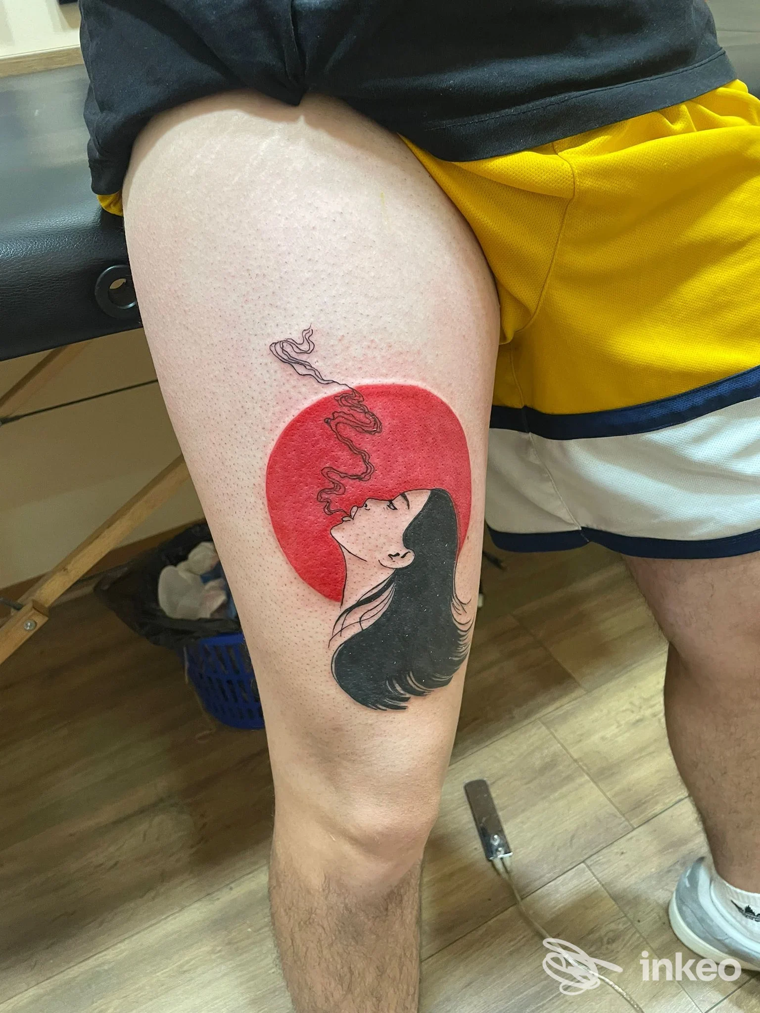 Tatuaggio su coscia: volto femminile stilizzato davanti a un cerchio rosso. Hell Yes tattoo shop, Lido di Ostia.
