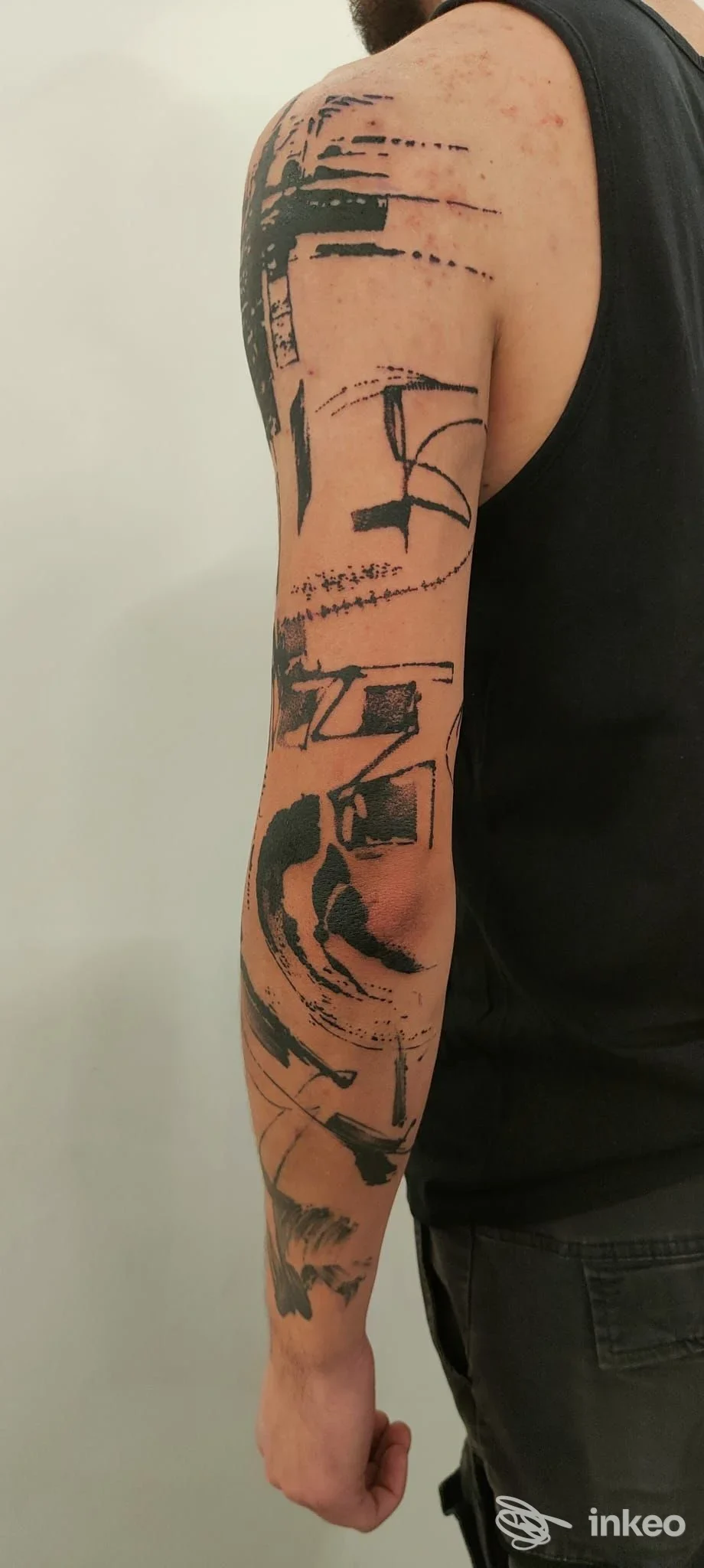 Manica astratta in nero su braccio e spalla di una persona, con tratti graffiati e blocchi pieni; foto fornita da Hannibal Tattoo, Roma.
