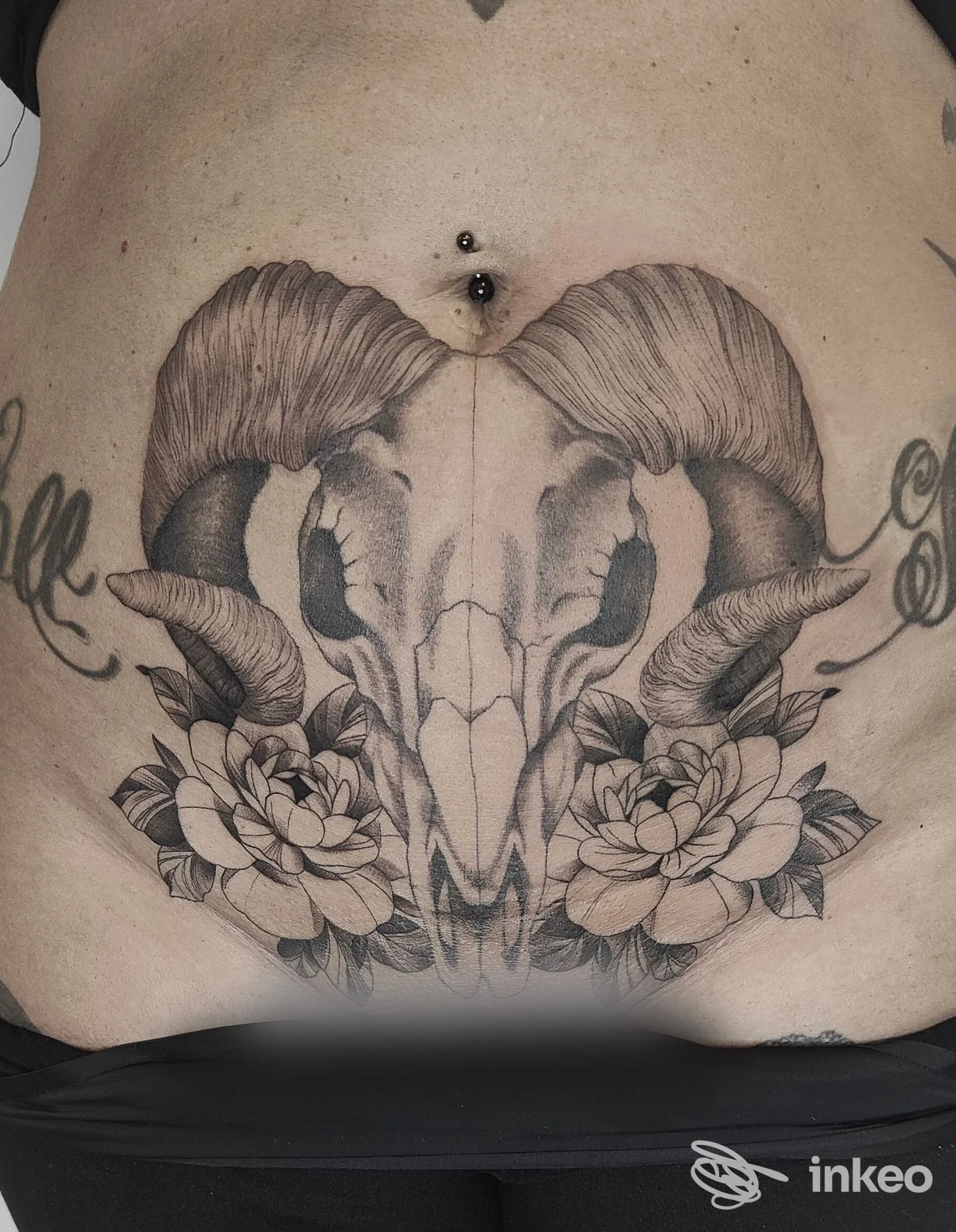 Tatuaggio addominale a Roma presso Indelible Art tattoo studio: teschio di montone con corna e fiori, con piercing all'ombelico.