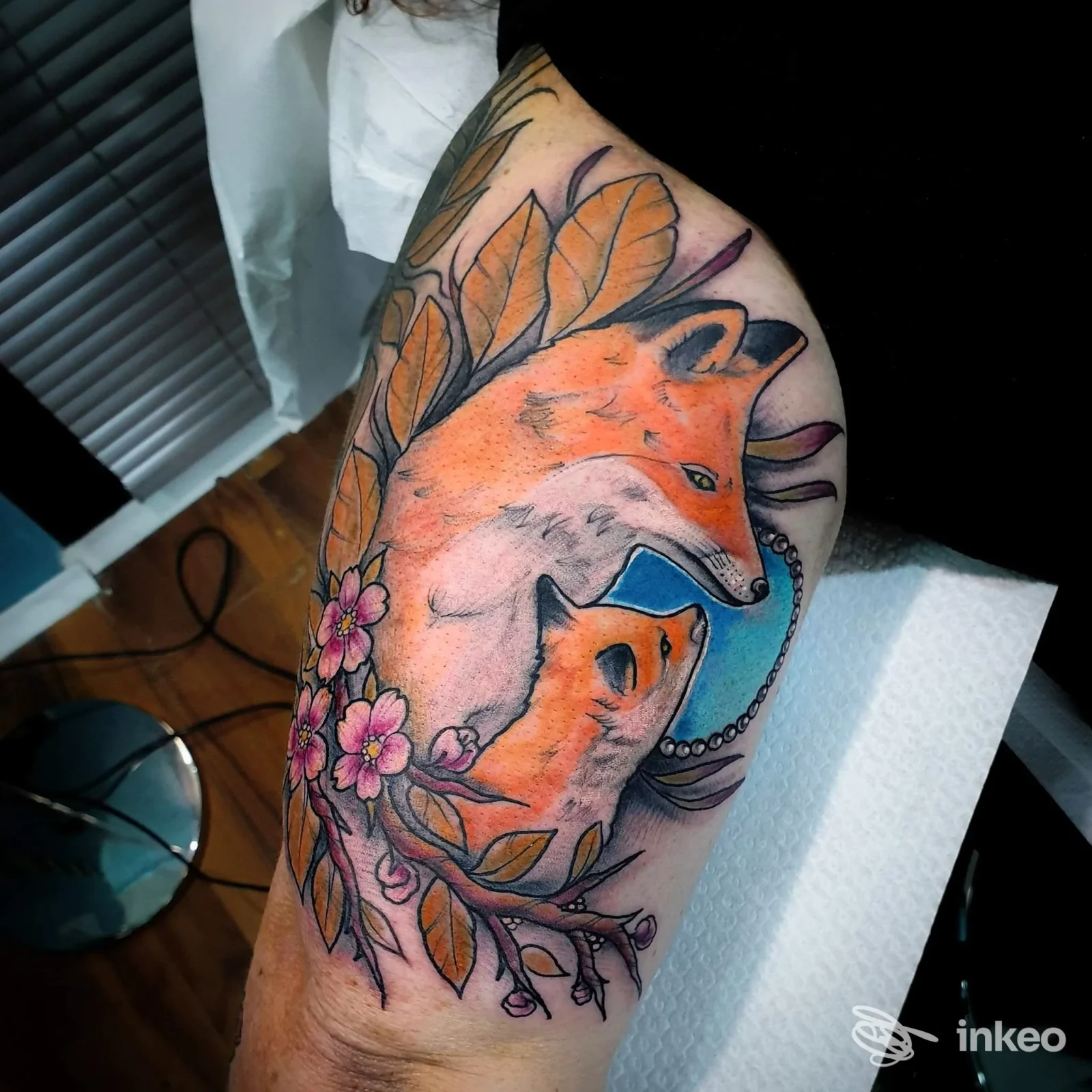Tatuaggio a colori di due volpi con fiori e foglie sul braccio/spalla, foto caricata da L'altra Metá Tattoo Shop, Gaeta.