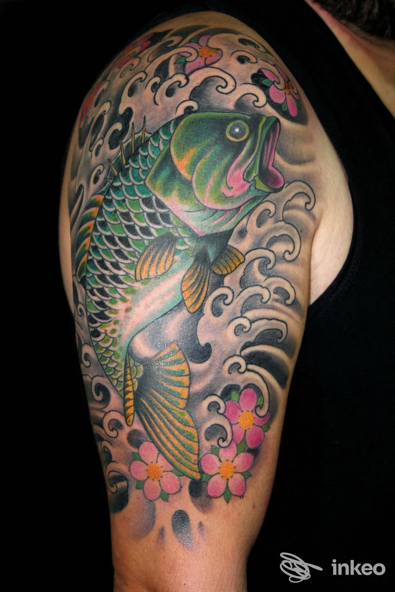 Tatuaggio su braccio superiore con carpa colorata, onde e fiori — immagine fornita da La Bottega dei Tatuaggi, Lido di Ostia.