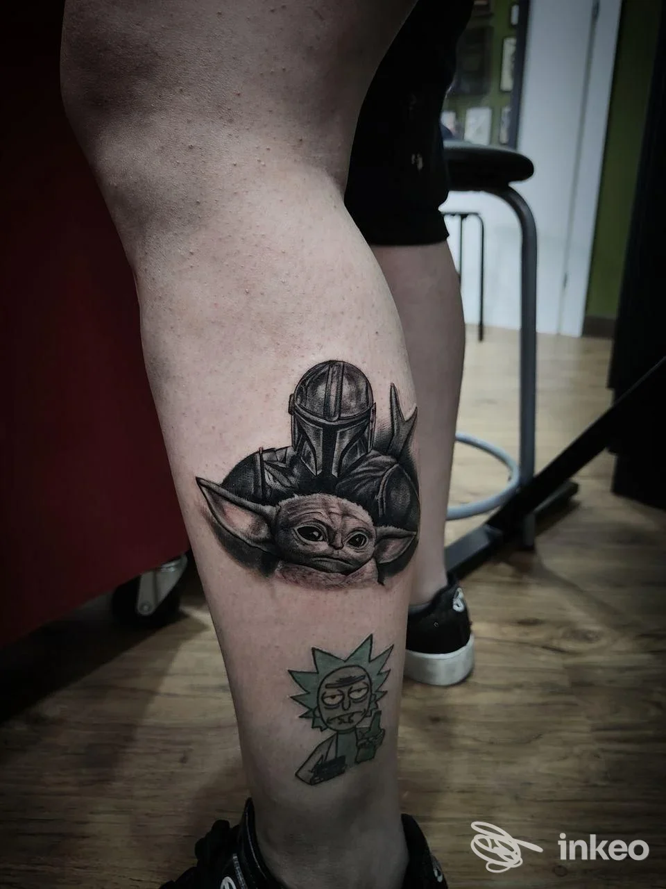 Dettaglio di due tatuaggi sul polpaccio: ritratto in bianco e nero del Mandaloriano con Grogu e personaggio colorato sotto. Lucky Tattoo and Piercing, Roma.