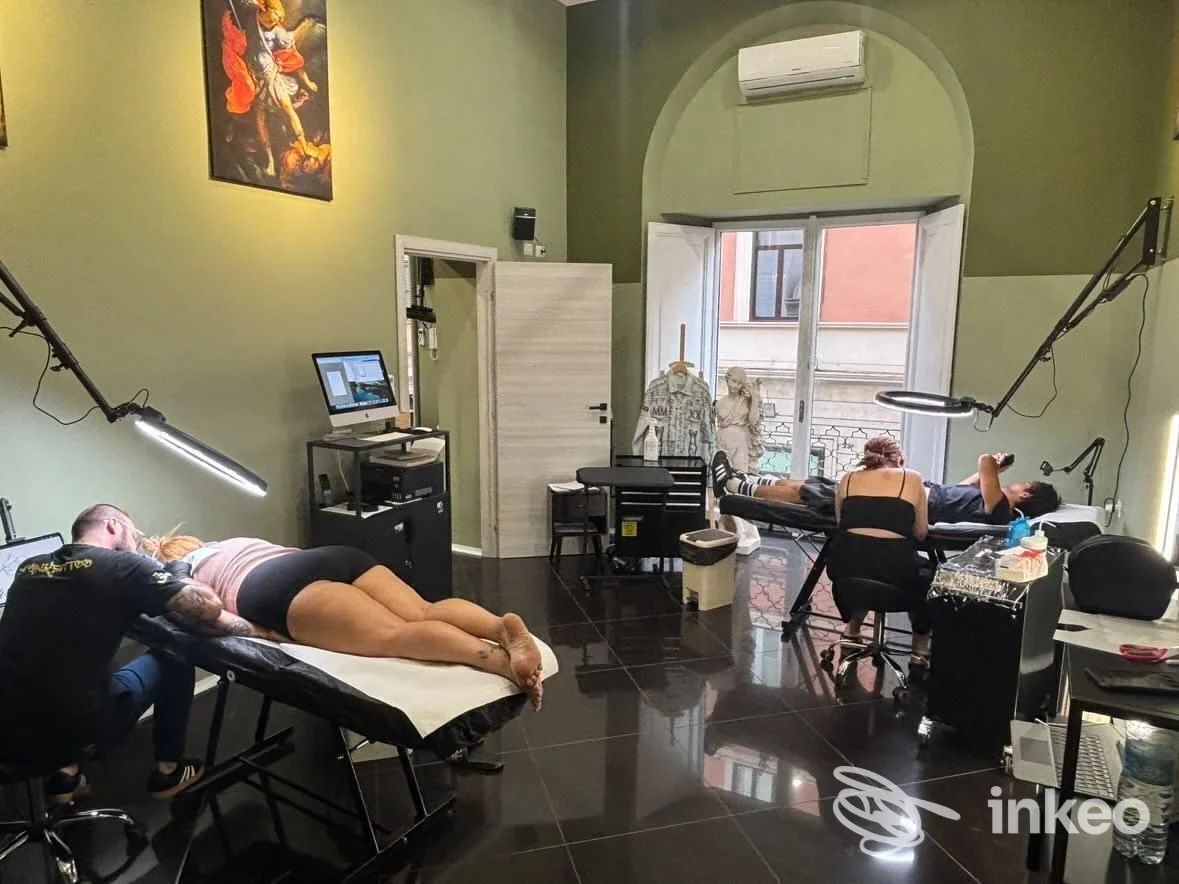 Interno di MAXIMO Tattoo Studio a Roma con due clienti su lettini mentre tatuatori eseguono lavori su schiena e fianchi.