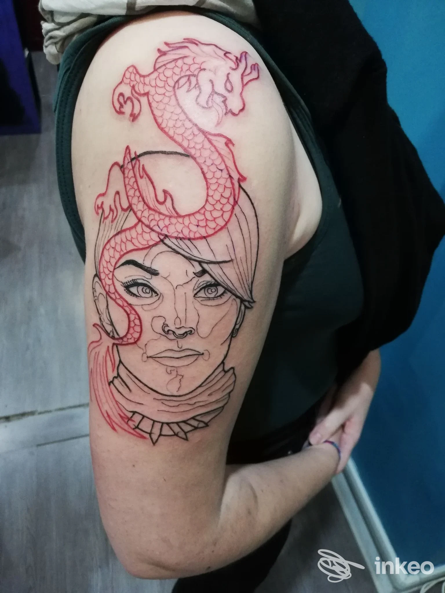 Tatuaggio su spalla con volto stilizzato in nero e drago rosso, La Laguna delle Sirene Tattoo, Roma.