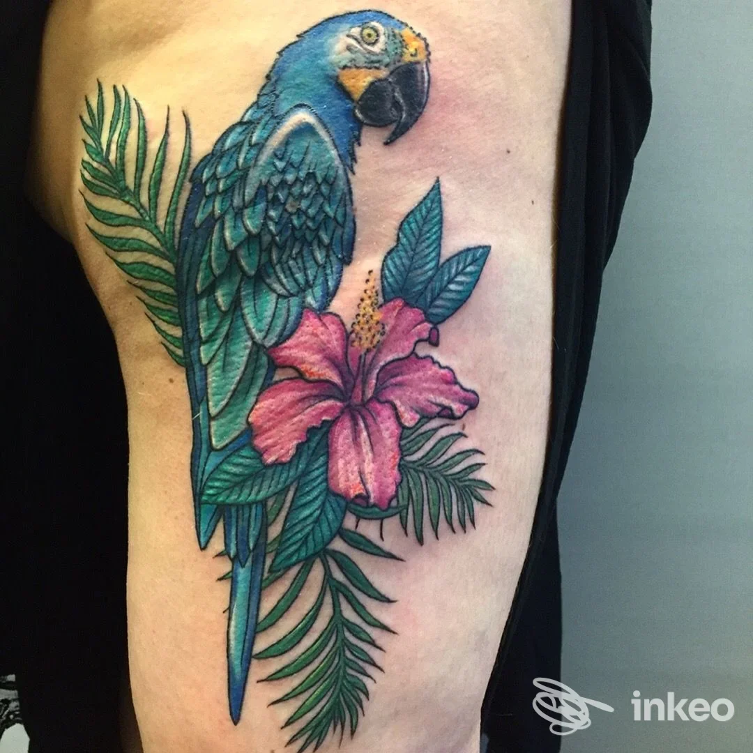 Grande tatuaggio a colori di pappagallo con foglie tropicali e ibisco sul fianco/coscia, eseguito da Roma Nord Tattoo, Roma.