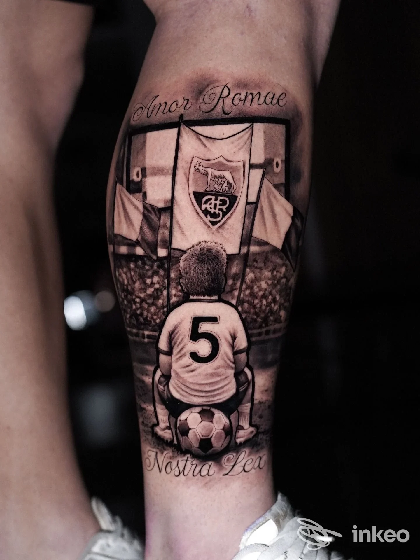 Tatuaggio realistico su polpaccio raffigurante un bambino con numero 5 e bandiere di squadra, realizzato da PHILIA TATTOO ROMA a Roma.