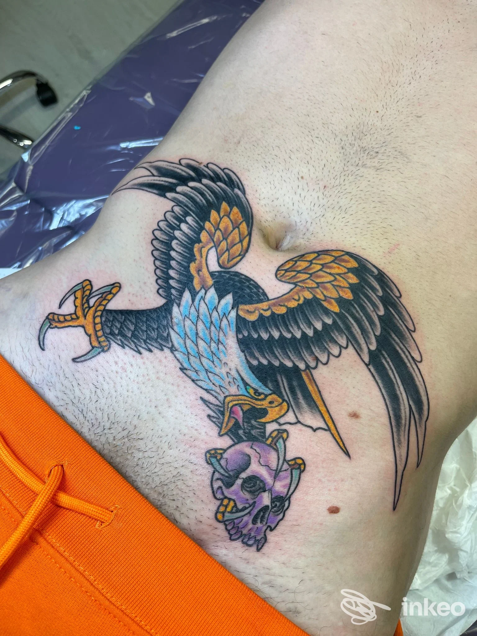 Tatuaggio neo-tradizionale di un uccello che afferra un teschio sul fianco, scatto di Psycho Tattoo Studio a Roma.
