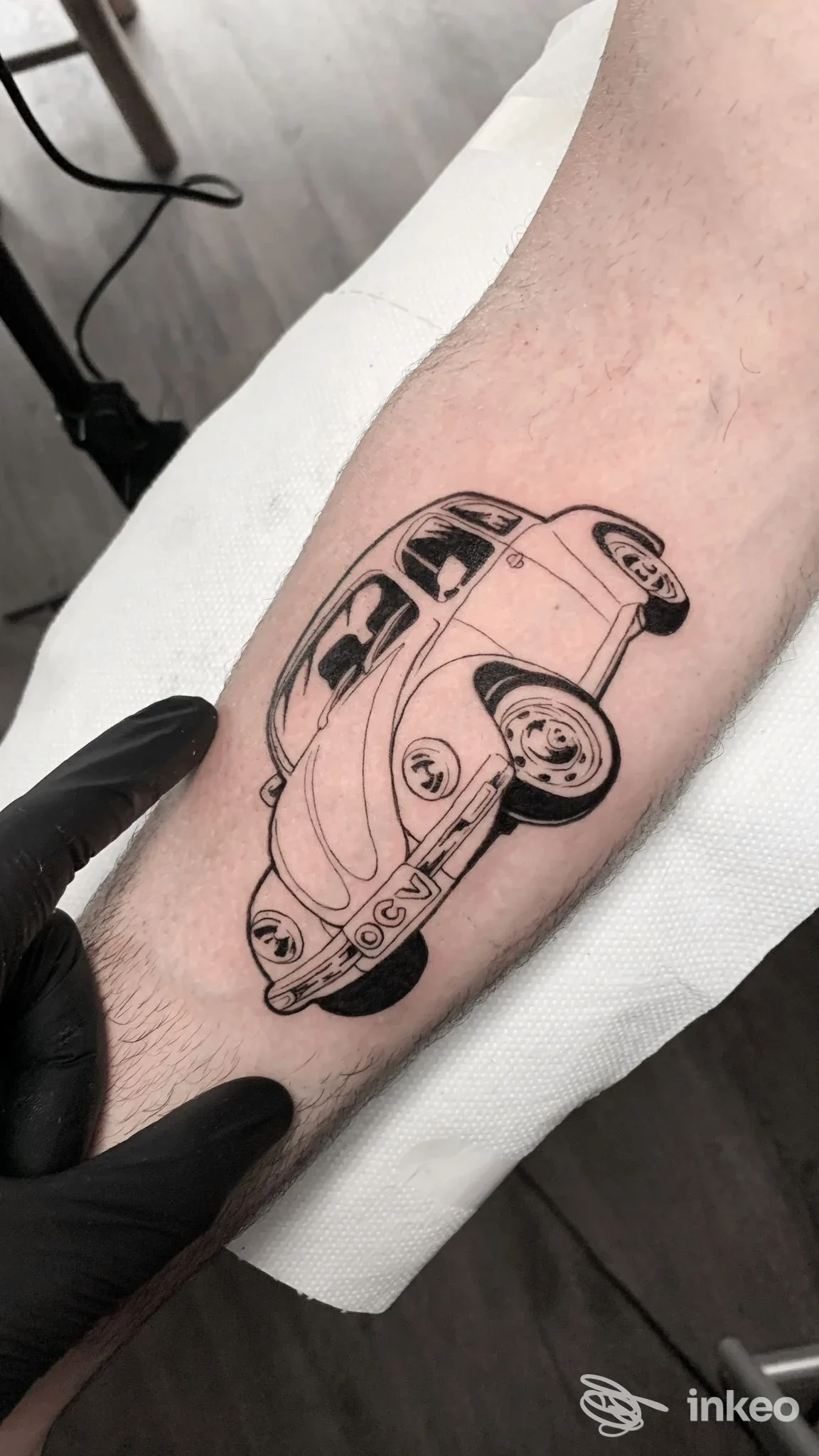 Tattoo su pelle raffigurante un'auto VW Maggiolino stilizzata, in bianco e nero, sulla gamba, sc ATT. Studio Black Fox Tattoo Studio.